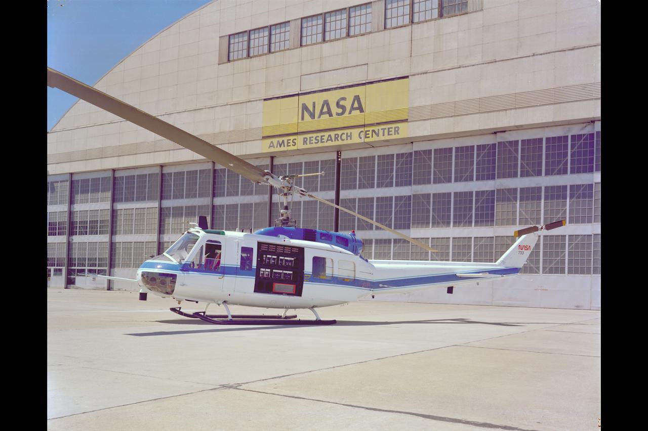 UH-IH Helicopter (NASA-733) with side door opened displaying STOLAND instruments parked in front of the NASA Hangar.