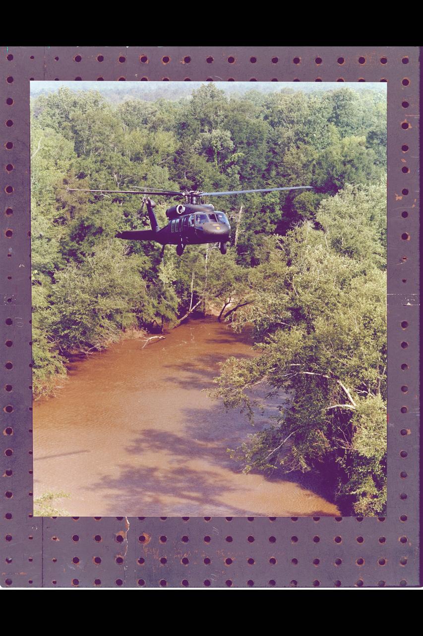 Army UH-60 Blackhawk helicopter flying Nap of the Earth in waterway of heavely wooded terrain.