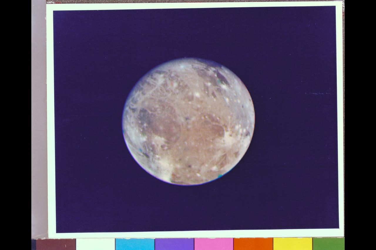 2:30 pm Photographer : JPL Range : 2.6 million km. ( 1.6 million miles ) Ganymede is Jupiter's largest satellite ( or moon ) With a radius of about 2600 km., about 1.5 times that of our moon, Ganymede has a bulk density of about 2.0 g/cc, almost half that of our moon, and is probably composed of rock and ice. The large dark regions, in the northeast quadrant, and the white spots, resemble features found on the moon, mare and impact respectively. The long white filaments resemble rays associated with impacts on the lunar surface. The various colors, other than the several blue, green, & orange dots, which are markings on the camera used for pointing determinations and are not physical markings, probably represent differing surface materials.