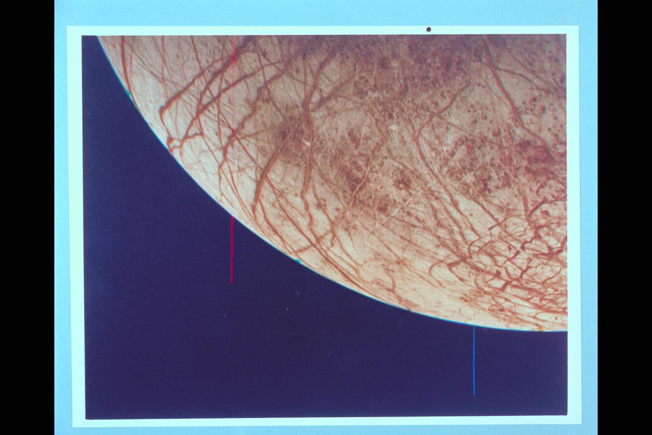 P-21760 C This color image of the Jovian moon Europa, which is the size of our moon, is thought to have a crust of ice perhaps 100 kilometers thick which overlies the silicate crust. The complex array of streaks indicate that the crust has been fractured and filled by materials from the interior. The lack of relief, any visible mountains or craters, on its bright limb is consistent with a thick ice crust. In contrast to its icy neighbors, Ganymede and Callisto, Europa has very few impact craters. One possible candidate is the small feature near the center of this image with radiating rays and a bright circular interior. The relative absence of features and low topography suggests the crust is young and warm a few kilometers below the surface. The tidal heating process suggested for Io also may be heating Europa's interior at a lower rate.