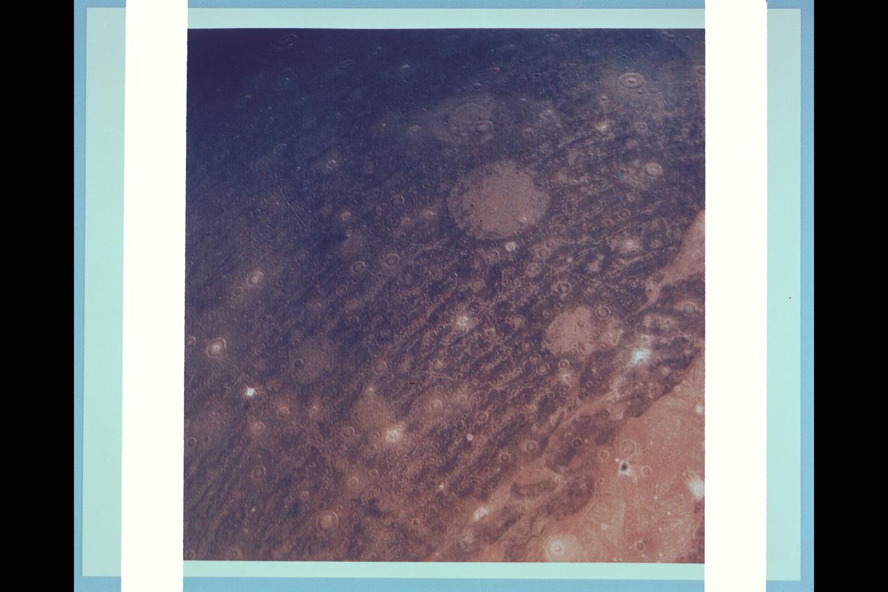 P-21761 C Range: 313,000 kilometers (194,000 miles) This color reconstruction of part of the northern hemisphere of Ganymede shows a scene approximately 1,300 kilometers (806 miles) across. It shows part of dark, densely cratered block which is bound on the south by lighter, and less cratered grooved terrain. The dark blocks are believed to be the oldest parts of Ganymede's surface. Numerous craters are visible, many with central peaks. The large bright circular features have little relief and are probably the remnants of old, large craters that have been annealed by flow of the icy near-surface material. The closely-spaced arcuate, linear features are probably analogous to similiar features on Ganymede which surround a large impact basin. The linear features here may indicate the former presence of a large impact basin to the southwest.