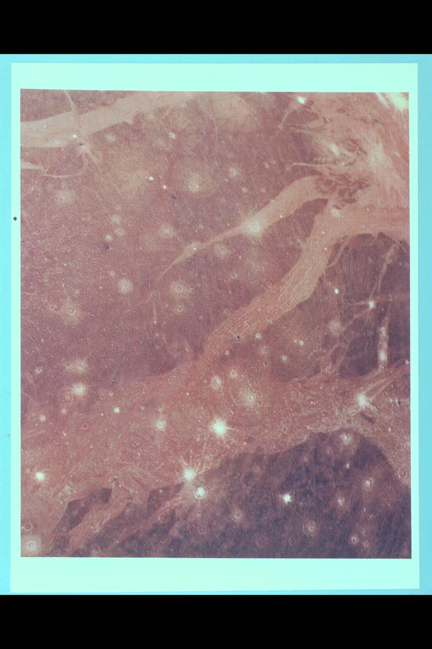 Range :  312, 000 kilometers (195,000 miles) This photo of Ganymede (Ice Giant) was taken from Voyager 2 and shows features down to about 5 to 6 kilometers across.  Different types of terrain common on Ganymede's surface are visible.  The boundary of the largest region of dark ancient terrain on Ganymede can be seen to the east (right), revealing some of the light linear features which may be all that remains of a large ancient impact structure similar to the large ring structure on Callisto.  The broad light regions running through the image are the typical grooved structures seen within another example of what might be evidence of large scale lateral motion in Ganymede's crust.  The band of grooved terrain (about 100 kilometers wide) in this region appears to be offset by 50 kilometers or more on the left hand edge by a linear feature perpendicular to it.  A feature similar to this one was previously discovered by Voyager 1.  These are the first clear examples of strike-slip style faulting on any planet other than Earth.  Many examples of craters of all ages can be seen in this image, ranging from fresh, bright ray craters to large, subdued circular markings thought to be the 'scars' of large ancient impacts that have been flatteded by glacier-like flows.