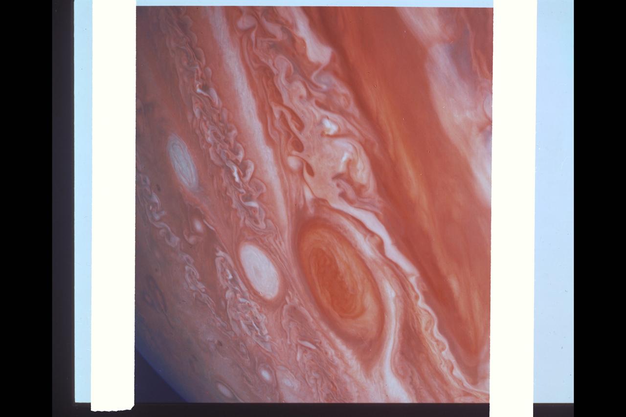 Range :  6 Million km. ( 3.72 million miles ) This photograph of Jupiter, shot from Voyager 2, shows the equator to the southern polar latitudes, near the Great Red Spot. The white oval that appears here is different from the one seen in a similiar position when voyager 1  passed years before. The region of white clouds now extends from east of The Red Spot and around it's northern boundary, preventing small cloud vortices from circling the feature. The disturbed region west of The Red Spot has also changed since Voyager1. It shows more small scale structure and cloud vortices being formed out of the wave structures.