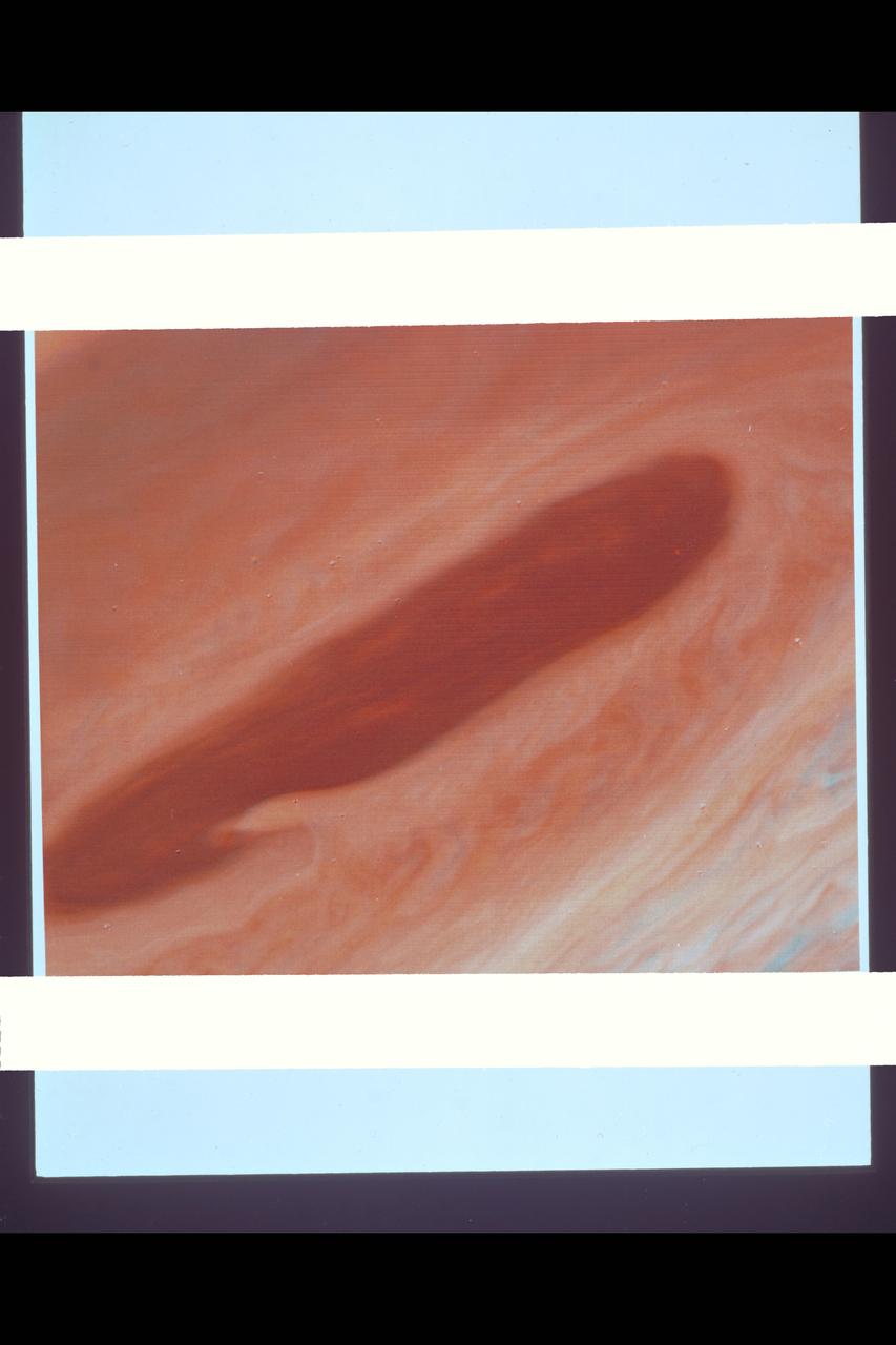 Range :  3.2 million km This image returned by Voyager 2 shows one of the long dark clouds observed in the North Equatorial Belt of Jupiter.  A high, white cloud is seen moving over the darker cloud, providing an indication of the structure of the cloud layers.  Thin white clouds are also seen within the dark cloud.  At right, blue areas, free of high clouds, are seen.