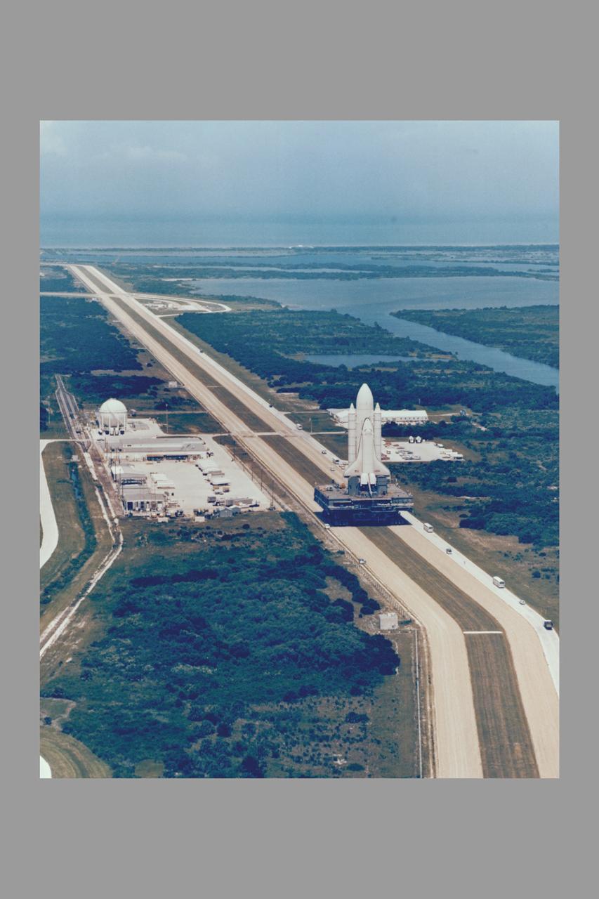 Space Shuttle Orbiter Enterprise, mated to a 15-story-tall external propellant tank and twin inert solid rocket boosters on top of a Mobile Launcher Platform, is rolled back to the Vehicle Assembly Building from Lauch Complex 39's Pad A July 23 at the completion of nearly three months of fit and function checks at the shuttle launch site as part of the exercise designed to help clear the way for the liftoff of its sister ship Columbia.  The massive Crawler Transporter began moving its 11 million pound load the 3.5 miles from pad A to the VAB at 10:23 a.m. and reached the doorway to High Bay 1 at 3:48p.m.  following serveral days of fit checks of modified extermiable platforms in the assembly bay, the nonlaunchable shuttle will be destacked.  Enterprise will be returned to Rockwell International and stripped of parts for integration into orbiter destined for space, while the external tank and solid booster will be returned to their respective prime contractors and refurbished for use on a later shuttle mission.