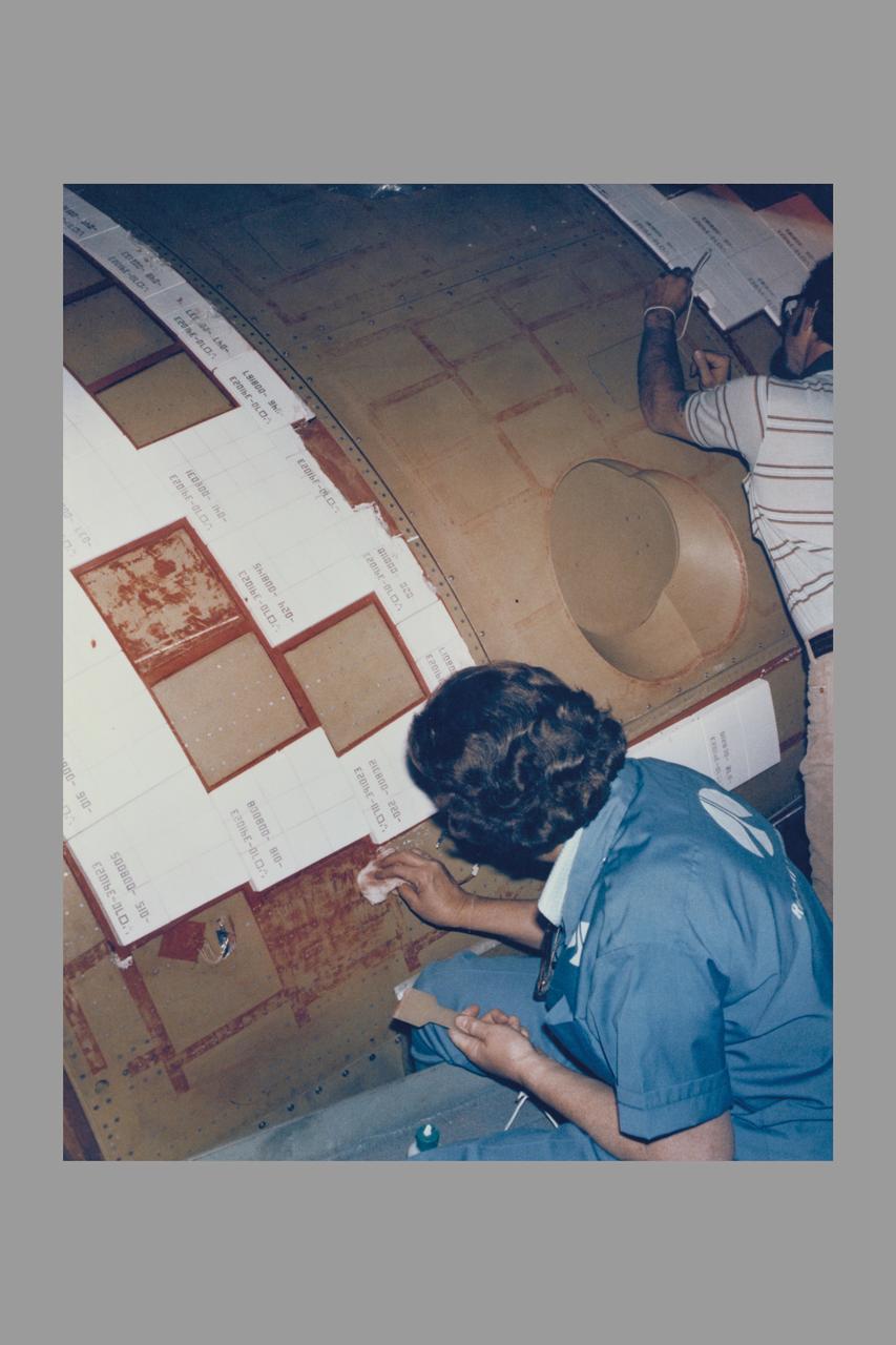 ROCKWELL INTERNATIONAL TECHNICIANS MOUNT SOME OF THE NEARLY 8,000 CERAMIC-COATED TILES THAT REMAIN TO BE INSTALLED ON THE EXTERNAL SURFACES OF THE SPACE SHUTTLE ORBITER COLUMBIA TO COMPLETE THE THERMAL PROTECTION SYSTEM THAT WILL ABSORB THE INTENSE HEAT OF REENTERING THE EARTH'S ATMOSPHERE AFTER A MISSION IN SPACE. TILE INSTALLATION IS DONE ON AN AROUND-THE-CLOCK BASIS IN THE ORBITER PROCESSING FACILITY WHERE COLUMBIA, THE FIRST IN A NEW BREED OF MANNED, REUSABLE SPACECRAFT, IS BEING READIED FOR THE FIRST LAUNCH OF THE SPACE SHUTTLE LATER THIS YEAR.