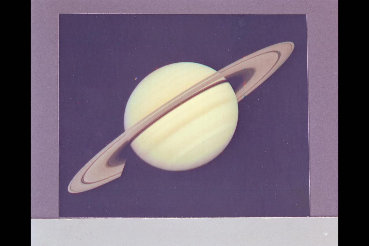 Range :  34 million km. ( 21.1 million miles) P-22993C This Voyager 1 photograph of Saturn was taken on the last day it could be captured within a single narrow angle camera frame as the spacecraft neared the planet for it's closest approach on Nov. 12, 1980. Dione, one of Saturn's innermost satellites, appears as three color spots just below  the planet's south pole. An abundance of previously unseen detail is apparent in the rings. For example, a gap in the dark, innermst ring, C-ring or Crepe Ring, is clearly shown. Also, material is seen inside the relatively wide Cassini Division, seperating  the middle, B-ring from the outermost ring, the A-ring. The Encke division is shown near the outer edge of A-ring. The detail in the ring's shadows cast on the planet is of particular interest. The broad dark band near the equator is the shadow of B-ring. The thinner, brighter line just to the south is the shadow  of the less dense A-ring.