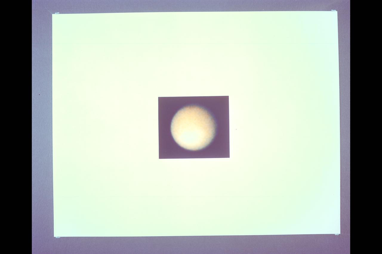 Range :  12 million km. ( 7.56 million miles) P-23057C & BW This Voyager 1 photograph of Titan, the largest of Saturn's 14 known satellites, shows little more than the upper layers of clouds covering the moon. The orange colored haze, is believed to be composed of photochemically produced hydrocarbons, hides Titan's solid surface from Voyager's camera. Some weak shadings in the clouds are becoming visible. However, note that the satellite's southern, lower, hemisphere is brighter than the northern. It is not known whether these subtle shadings are on the surface or are due to clouds below a high haze layer.