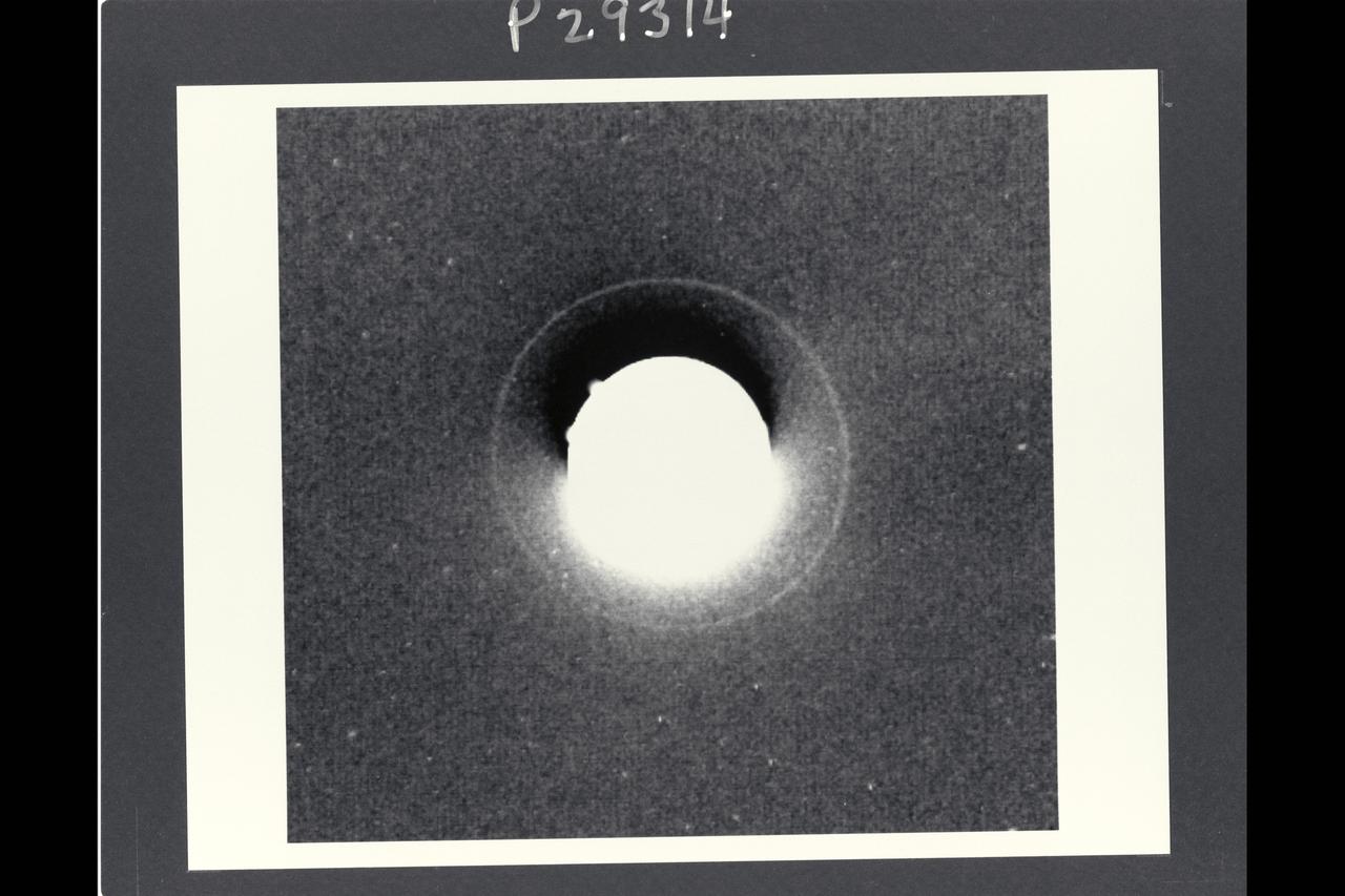Range:  72.3 million km. ( 44.9 million miles ) P-29314B/W This Voyager 2 photograph of Uranus shows the planets outermost, or epsilon, ring.  This is a computerized summation of six images shot by the narrow angle camera. It is the first photo to show the epsilon ring unblurred by Earth's atmosphere. The Epsilon ring, some 51,200 km. ( 31,800 miles )  from the planets center, is the most prominent of Uranus' nine known rings. Ground based observations of stellar occulations by the rings have determined that the Epsilon ring is eccentric, or elliptical, with its widest portion  about 100 km. ( 60 miles ) wide and its narrowest portion about 20 km. (12 miles ). Estimates of the rings brightness suggest that it is also very dark, with a reflectance of only 1 or 2  percent and a probable  composition of carbonaceous material similiar to that on dark asteroids and the dark side of Saturn's moon Lapetus. Because the ring is so narrow and dark, at this range,  the Voyager camera could not  resolve even the widest part,  resulting in long exposure times so obtain a good image. six exposures of 11 or 15 second duration were added together by computer to produce this image.  In this image, the central  portion is greatly overexposed. Various artifacts due to electronic effects  and image proccessing can be seen in the central portion of the frame, including the dark image just above the planets image, the diffuse brightening below it and the small, bright projection from the edge of the planet in the upper left. The ring is distinctly less prominent in the lower left portion and more prominent in the upper right. This is in agreement with the predicted locations of the narrow and wide portions of the ring, respectively.