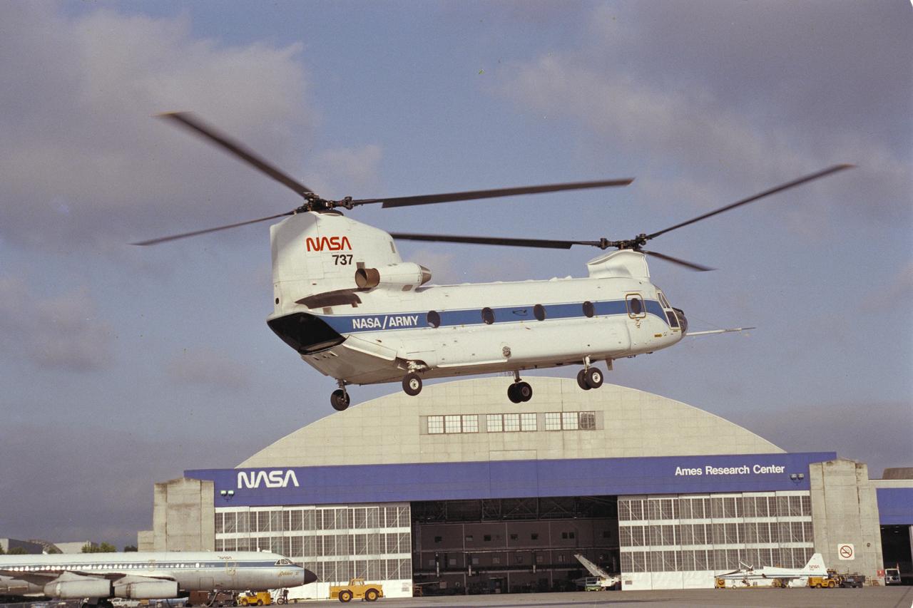 CH-47B (NASA-737) in flight with NASA Ames Research Center Hangar in the background.