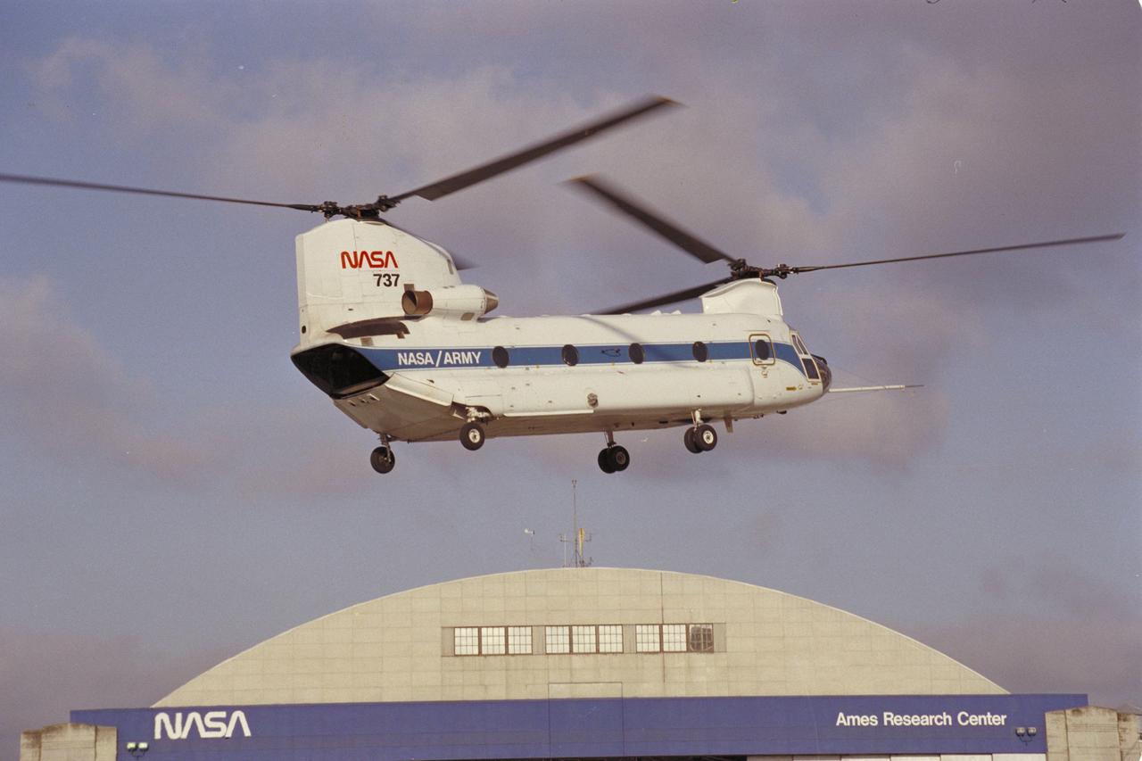 CH-47B (NASA-737) in flight with NASA Ames Research Center Hangar in the background.