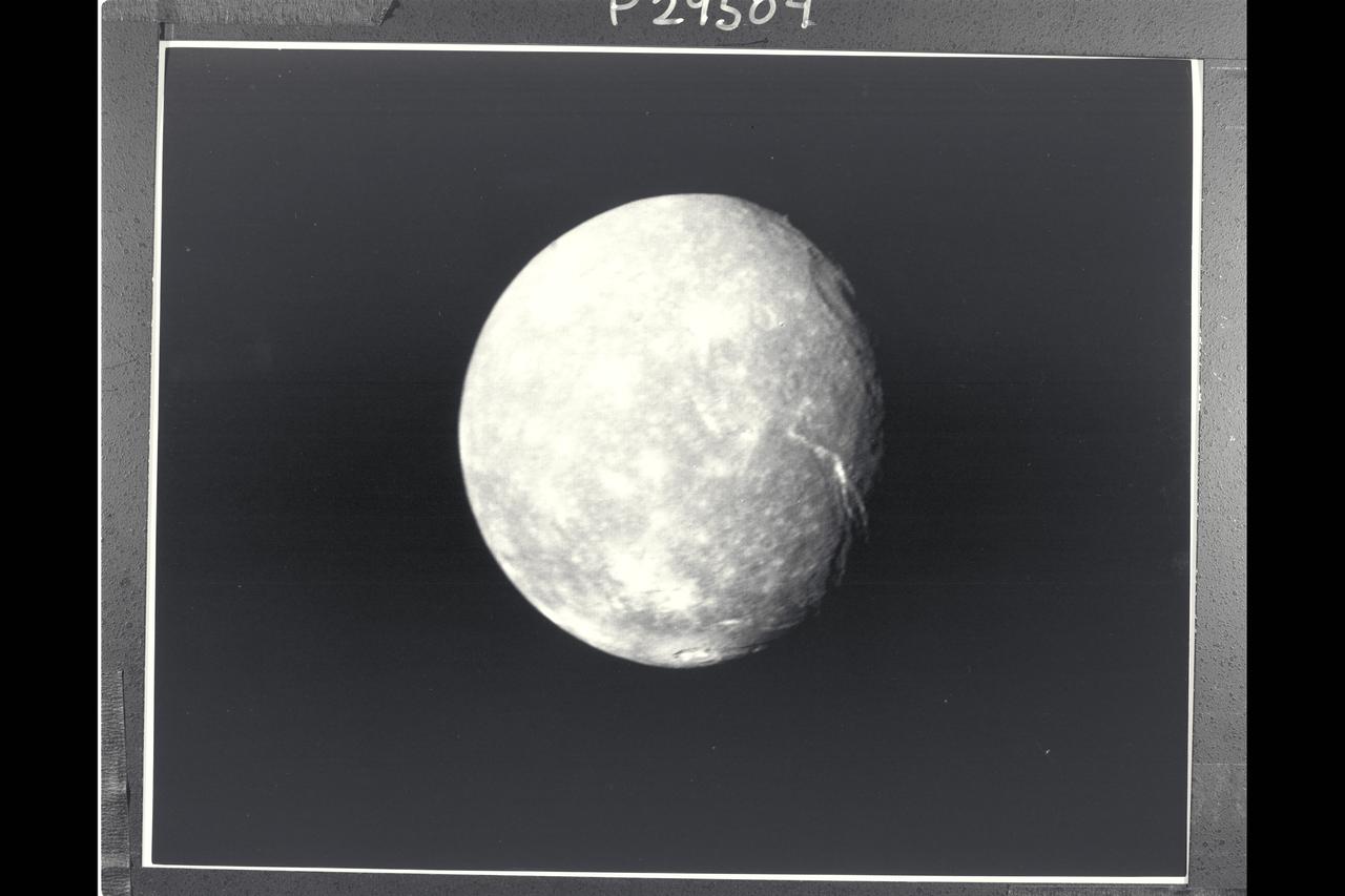 P-29504BW Range: 500,000 kilometers (300,000 miles) This full-disk view of Uranus' moon Titania in the early morning hours, a clear-filter image returned by the Voyager narrow-angle camera, shows many circular depressions-probably impact craters. Other bright spots are distinguished by radiating rays and are probably halo craters that mark relatively more recent impacts. Even more interesting are the linear troughs (right) that are probably fault canyons. The troughs break the crust in two directions, an indication of some tectonic extension of Titania's crust. These features indicate that this icy satellite has a dynamic, active interior. Titania is about 1,600 km (1,000 mi) in diameter; the resolution of this image is about 9 km (6 mi).