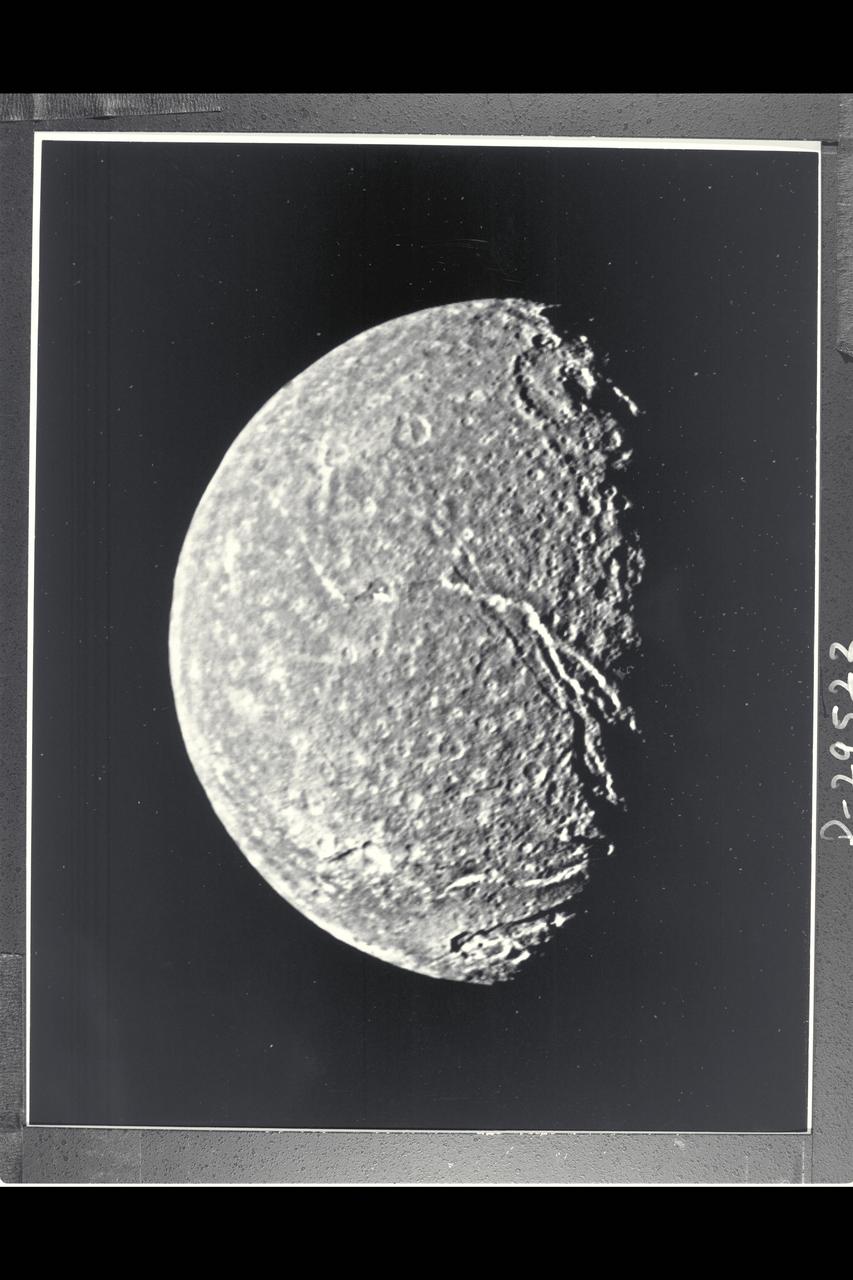 P-29522BW Range: 369,000 kilometers (229,000 miles) This is the highest-resolution picture of Titania returned by Voyager 2. The picture is a composite of two images taken through the clear-filter of Voyager's narrow-angle camera. The resolution of this image is 13 km (8 mi). Titania is the largest satellite of Uranus, with a diameter of little more than 1,600 km (1,000 mi). Abundant impact craters of many sizes pockmark the ancient surface. The most prominant features are fault valleys that stretch across Titania. They are up to 1,500 km (nearly 1,000 mi) long and as much as 75 km (45 mi) wide. In valleys seen at right center, the sunward-facing walls are very bright. While this is due partly to the lighting angle, the brightness also indicates the presence of a lighter material, possibly young frost deposits. An impact crater more than 200 km (125 mi) in diameter distinguishes the very bottom of the disk; the crater is cut by a younger fault valley more than 100 km (60 mi) wide. An even larger impact crater, perhaps 300 km (180 mi) across, is visible at top.
