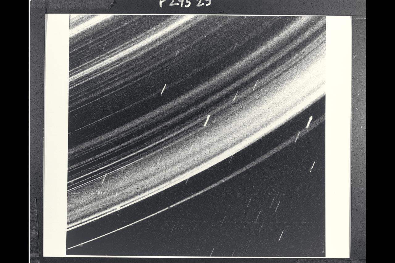Range :  236,000 km. ( 147,000 mi. ) Resolution :  33 km. ( 20 mi. ) P-29525B/W This Voyager 2 image reveals a contiuos distribution of small particles throughout the Uranus ring system. This unigue geometry, the highest phase angle at which Voyager imaged the rings, allows us to see lanes of fine dust particles not visible from other viewing angles. All the previously known rings are visible. However, some of the brightest features  in the image are bright dust lanes not previously seen. the combination of this unique geometry and a long, 96 second exposure allowed this spectacular observation, acquired through the clear filter if Voyager 2's wide angle camera. the long exposure produced a noticable, non-uniform smear, as well as streaks due to trailed stars.