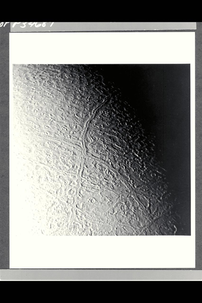 P-34689 Range : 130,000 km. ( 80,000 miles ) Smallest Resolvable Feature : 2.5 km or 1.5 miles This image of Neptune's moon Triton, shot by Voyager 2, is seen here. The long linear feature exteding vertically across the image is probably a graben -- a norrow down-dropped fault block about 35 km. or 20 miles across. The ridge in the center of the graben. The surrounding terrain is a relatively young icy surface with few impact craters.