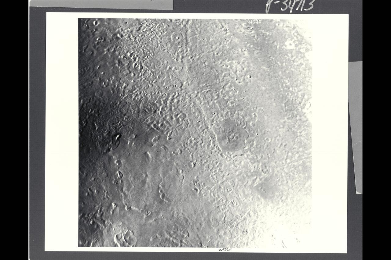 P-34713 This Voyager image of Triton reveals two kinds of mid-latitude terrain. Near the center and the lower half of the frame is a gently rolling terrain pock-marked with a modest number of impact craters. The density of impact craters is somewhat similiar to that found on the mare surface of Earth's moon. Crossing this rolling surface are narrow rifts, one of which grades into a chain of craters that probably are of collapse origin. In the upper right part of the frame is a smooth terrain with very sparse impact craters. This terrain evidently has been formed by flooding of the surface by low-viscosity fluids rather late in geologic time. One of the vents from which these fluids erupted probably is represented by a deep, elongate crater near the middle of the right side of the image. Two slightly dark regions underlain by late eruptive material also occur in the left half of the image. Apparent vents for these eruptions are marked by shallow depressiions, which may have been formed by drain back of material at the end of the eruptive episode.