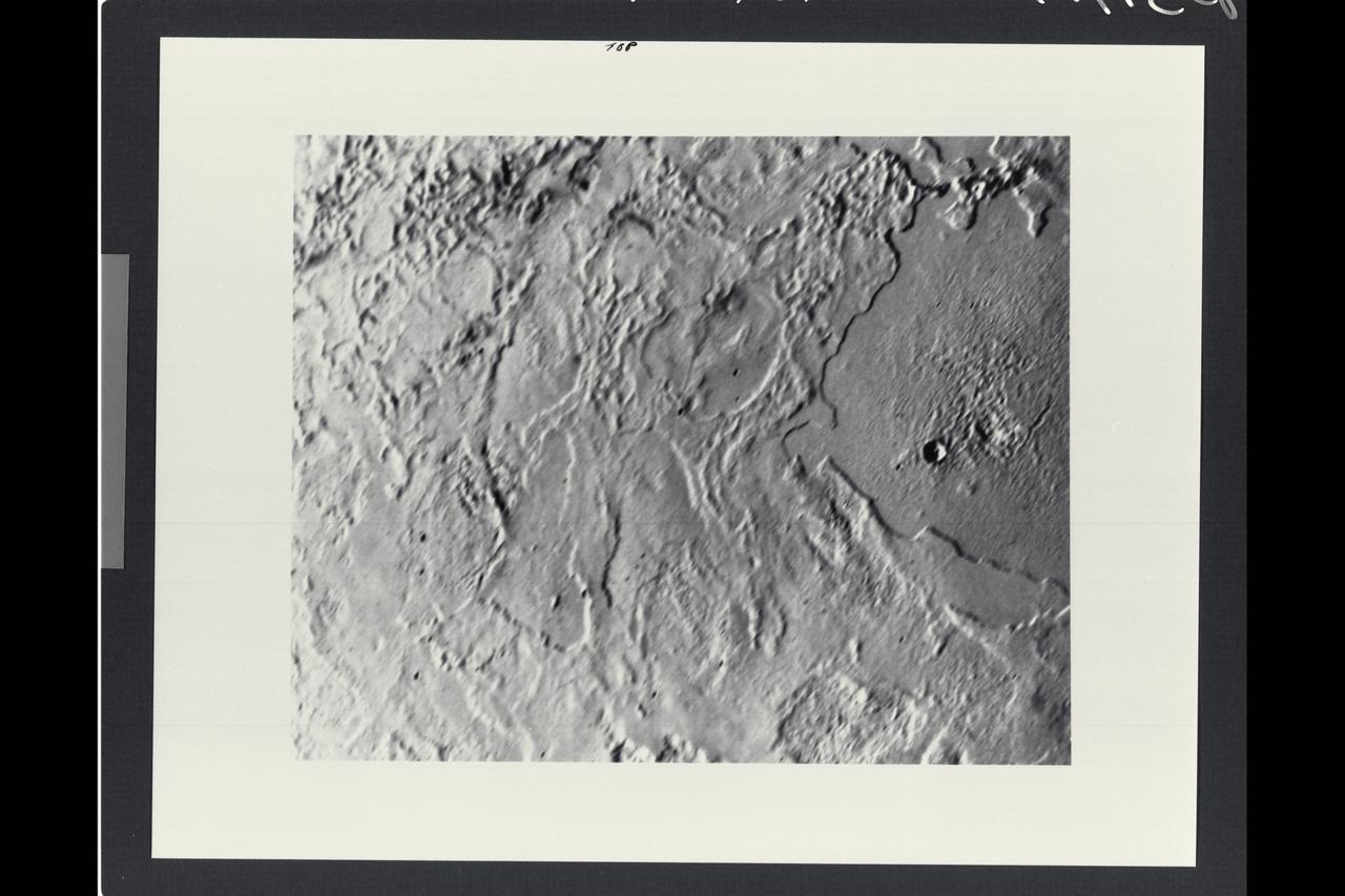 P-34717 Range: 80,000 kilometers (50,000 miles) This image taken by Voyager 2 of Neptune's largest satellite, Triton, shows an area in the northern hemisphere. The Sun is just above the horizon, so features cast shadows that accentuate height differences. The large, smooth area in the right-hand side of the image shows a single, fresh, impact crater. Otherwise there is no evidence of impacts such as those that have pocked the faces of most of the satellites Voyager 2 has visited. Many low cliffs in the area, bright where they face the Sun, and dark when they face away from it, suggest an intricate history for Triton. The cliffs might be due either to melting of surface materials or, possibly, caused by unusual fluid materials that flowed sometime in Triton's past.