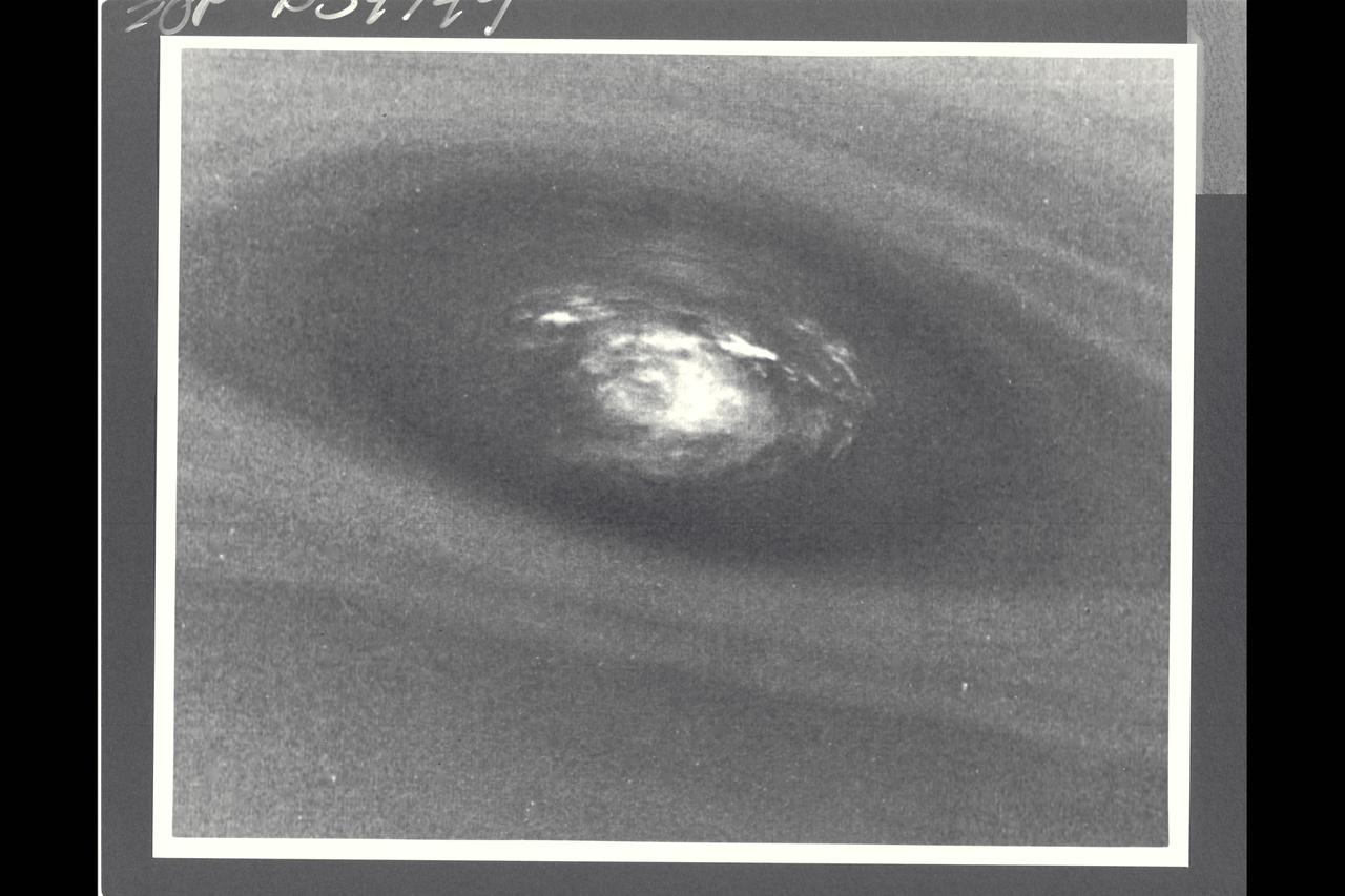 Voyager II Imagery; Neptune. This bulls-eye view of Neptune's small dark spot (D2) was obtained by Voyager 2's narrow-angle camera , when Neptune was within 1.1 million km (680,000 miles) of the planet. The smallest structures that can be seen are 20 km (12 miles) across. This unplanned photograph was obtained when the infrared spectrograph was mapping the  the highest-resolution view of the feature taken during the flyby. Banding surrounding the feature indicates unseen strong winds, while structues within the bright spot suggest both active upwelling of clouds and rotation about the center. A rotation rate has not yet been measured, but the v-shaped structure near the right edge of the bright area indicates that the spot rotates clockwise. Unlike the Great Red Spot on Jupiter, which rotates counterclockwise, if the D2 spot on Neptune rotates clockwise, the material will be descending in the dark oval region. The fact that infrared data will yield temperature information about the region above the clouds makes this observation especially valuable. The Voyager Mission is conducted by JPL for NASA's Office of Space Science and Applicaitons.  (JPL ref: P-34749  Voyager N-71) taken during the flyby. Banding surrounding the feature indicates unseen strong winds, while structures within the bright spot suggest both active upwelling of clouds and rotation about the center. A rotation rate has not yest been measured, but the Vv-sphped