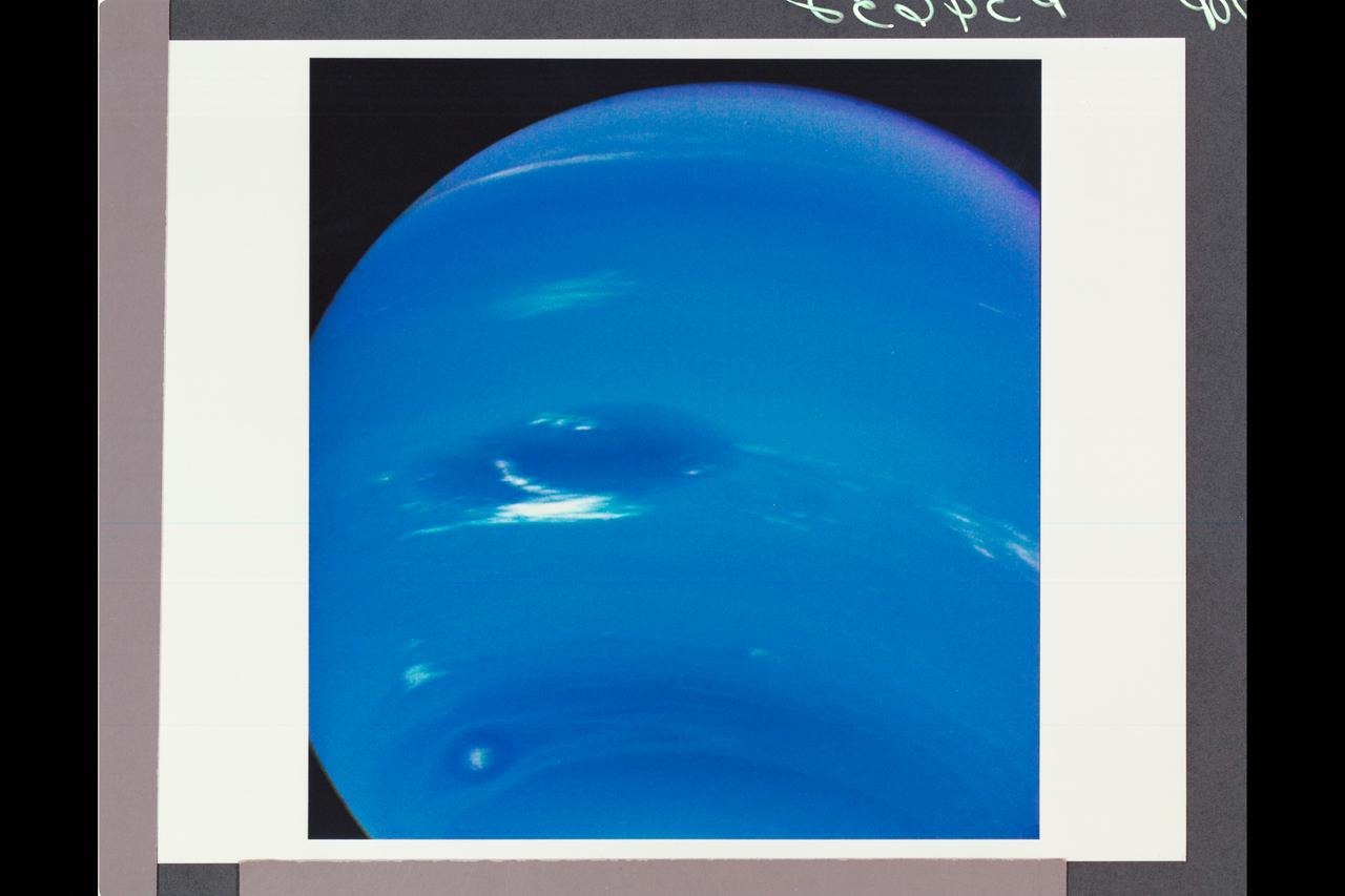 Voyager II Imagery - Neptune: This image of clouds in Neptune's atmosphere is the first that tests the accuracy of the weather forecast that was made eight days earlier to select targets for the Voyager narrow-angle camera.  Three of the four targeted features are visible in this photograph; all three are close to their predicted locations. The Great Dark Spot with its bright white companion is slightly to the left of center. The small bright Scooter is below and to the left, and the second dark spot with its bright core is below the Scooter. Strong eastward winds -- up to 400 mph -- cause the second dark spot to overtake and pass the larger one every five days.  The spacecraft was 6.1 million kilometers (3.8 million miles) from the planet at the time of camera shuttering, and the images use the orange, green and clear filters of the camera.  The Voyager Mission is conducted by JPL for NASA's Office of Space Science and Applications.   (JPL ref P-34632  Voyager 2 N-32C)