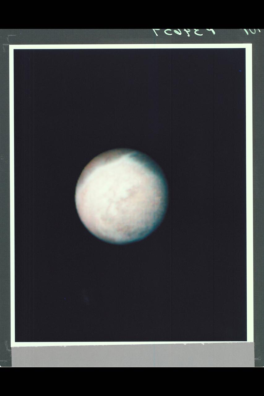 Range : 4 million km. ( 2.5 million miles ) P-34654 This Voyager 2 image of Neptune's satteltite Triton was made by combining images taken through the green, clear, and violet filters. The smallest feature seen are about 74 km, or 46 miles accross. The south pole of Triton is currently tipped toward the sun and it is summer in the southern hemisphere. The south pole is located about a quarter of the way up from the bottom if the image. The bright band near the top of the image nearly coincides with the equator of Triton. One prominent and several smaller bright, wispy streaks extend from the band into the darker northern hemisphere. The prominent wispy streak shows bluish-white color, while the darker northern hemisphere is reddish in color. This may indicate that the streak is freshly deposited frost while the red color in the northern hemisphere may result from methane frost that has been darkened by radiation. Individual markings appear to rotate with the satellite and retain their shapes indicating they are indeed surface features and not in the tenuous atmosphere.