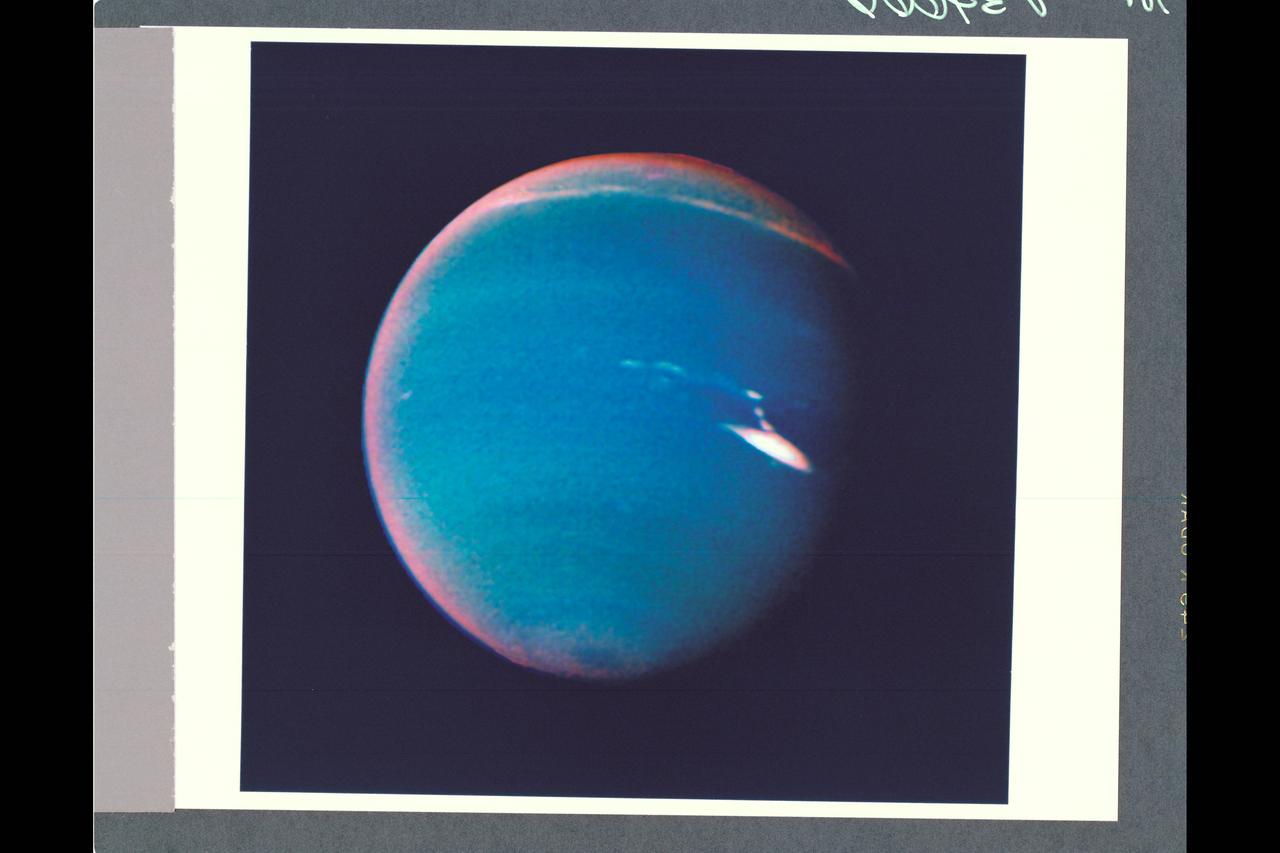 P-34666 This false color photograph of Neptune was reconstructed from two images taken by Voyager 2's wide angle camera, through the orange and two different methane filters. Objects that deep in the atmosphere are blue, while those at higher altitudes are white. Light at methane wavelengths is mostly absorbed in the deeper atmosphere. The bright, white feature is a high altitude cloud just south of the Great dark Spot. The hard, sharp inner boundary within the bright cloud is an artifact of computer processing on Earth. Other, smaller clouds associated with the Great Dark Spot are white or pink, and are also at high altitudes. Neptune's limb looks reddish because Voyager 2 is viewing it tangentially, and the sunlight is scattered back to space before it can be absorbed by methane. A long, narrow band of high-altitude clouds near the top of the image is located at 25 degrees north latitude, and faint hazes mark the equator and polor regions