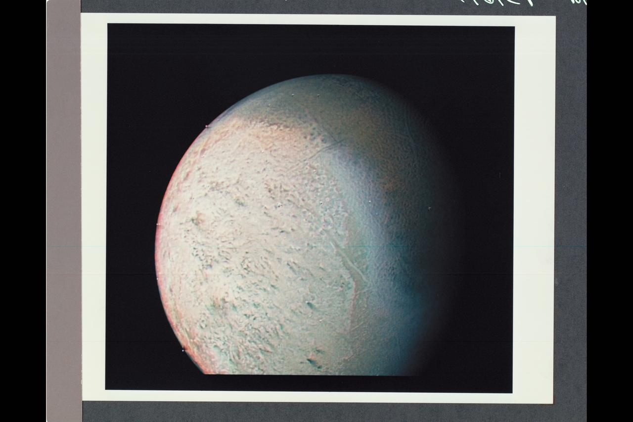 Range : 530,000 km (330,000 mi.) This color photo of Neptune's large satellite Triton has a resolution of about 10 km (6.2 mi), sufficient to begin to show topographic detail. The image was made from pictures taken through the green, violet and ultraviolet filters. In this technique, regions that are highly reflective in the ultraviolet appear blue in color. In reality, there is no part of Triton that would appear blue to the eye. The bright southern hemisphere of Triton, which fills most of this frame, is generally pink in tone as is the even brighter equatorial band. The darker regions north of the equator also tend to be pink or reddish in color.