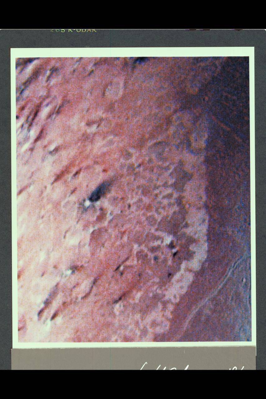 Range : 190,000 km ( 118,000 mi.) This false color image of Triton is a composite of images taken through the violet, green and ultraviolet filters. The smallest visible features are about 4 km (2.5 mi.) across. The image shows a geologic boundary between completely dark materials and patchy light/dark materials. A layer of pinkish material stretches across the center of the image. The pinkish layer must be thin because underlying albedo patterns show through. Several features appear to be affected by the thin atmosphere; the elongated dark streaks may represent particulate materials blown in the same direction by previaling winds, and the white material may be frost deposits. Other features appear to be volcanic deposits including the smooth, dark materials alongside the long, narrow canyons. The streaks themselves appear to originate from very small circular sources, some of which are white, like the source of the prominent streak near the center of the image. The sources may be small volcanic vents with fumarolic-like activity. The colors may be due to irradiated methane, which is pink to red, and nitrogen, which is white.