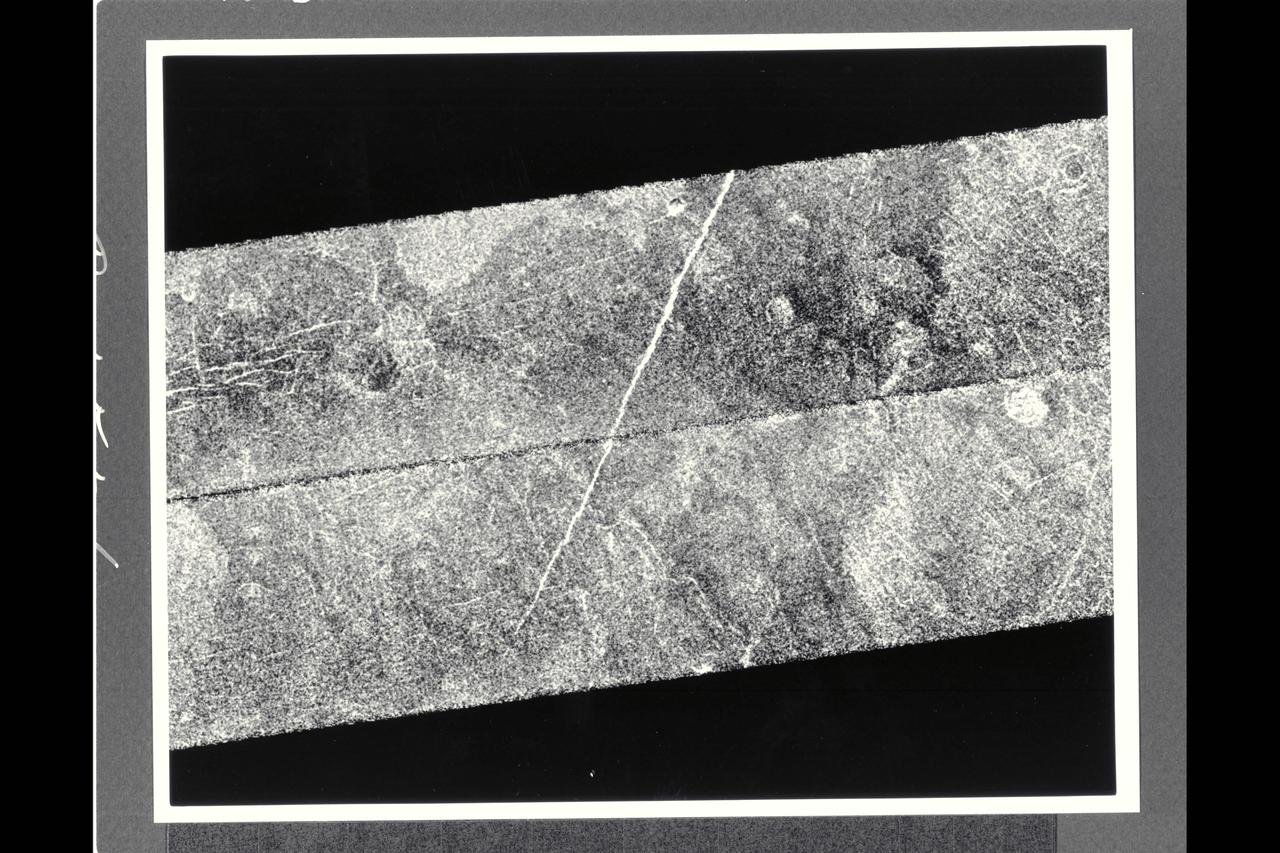 After traveling more than 1.5 billion km (948 million mi.), the Magellan spacecraft was inserted into orbit around Venus on Aug. 10, 1990.  This mosaic consists of adjacent pieces of two magellan image strips obtained in the first radar test.  The radar test was part of a planned In-Orbit Checkout sequence designed to prepare the magellan spacecraft and radar to begin mapping after Aug. 31.  The strip on the left was returned to the Goldstone Deep Space Network station in California; the strip to the right was received at the DSN in Canberra, Australia.  A third station that will be receiving Magellan data is locaterd near Madrid, Spain.  Each image strip is 20 km (12 mi.) wide and 16,000 km (10,000 mi.) long.  This mosaic is a small portion 80 km (50 mi.) long.  This image is centered at 21 degrees north latitude and 286.8 degrees east longitude, southeast of a volcanic highland region called Beta Regio.  The resolution of the image is about 120 meters (400 feet), 10 times better than revious images of the same area of Venus, revealing many new geologic features.  The bright line trending northwest-southeast across the center of the image is a fracture or fault zone cutting the volcanic plains.  In the upper lest corner of the image, a multiple-ring circular feature of probable volcanic origin can be seen,  approx. 4.27 km (2.65 mi.) across.  The bright and dark variations seen in the plains surrounding these features correspond to volcanic lava flows of varying ages.  The volcanic lava flows in the southern half of the image have been cut by north-south trending faults.  This area is similar geologically to volcanic deposits seen on Earth at Hawaii and the Snake River Plains in Idaho.