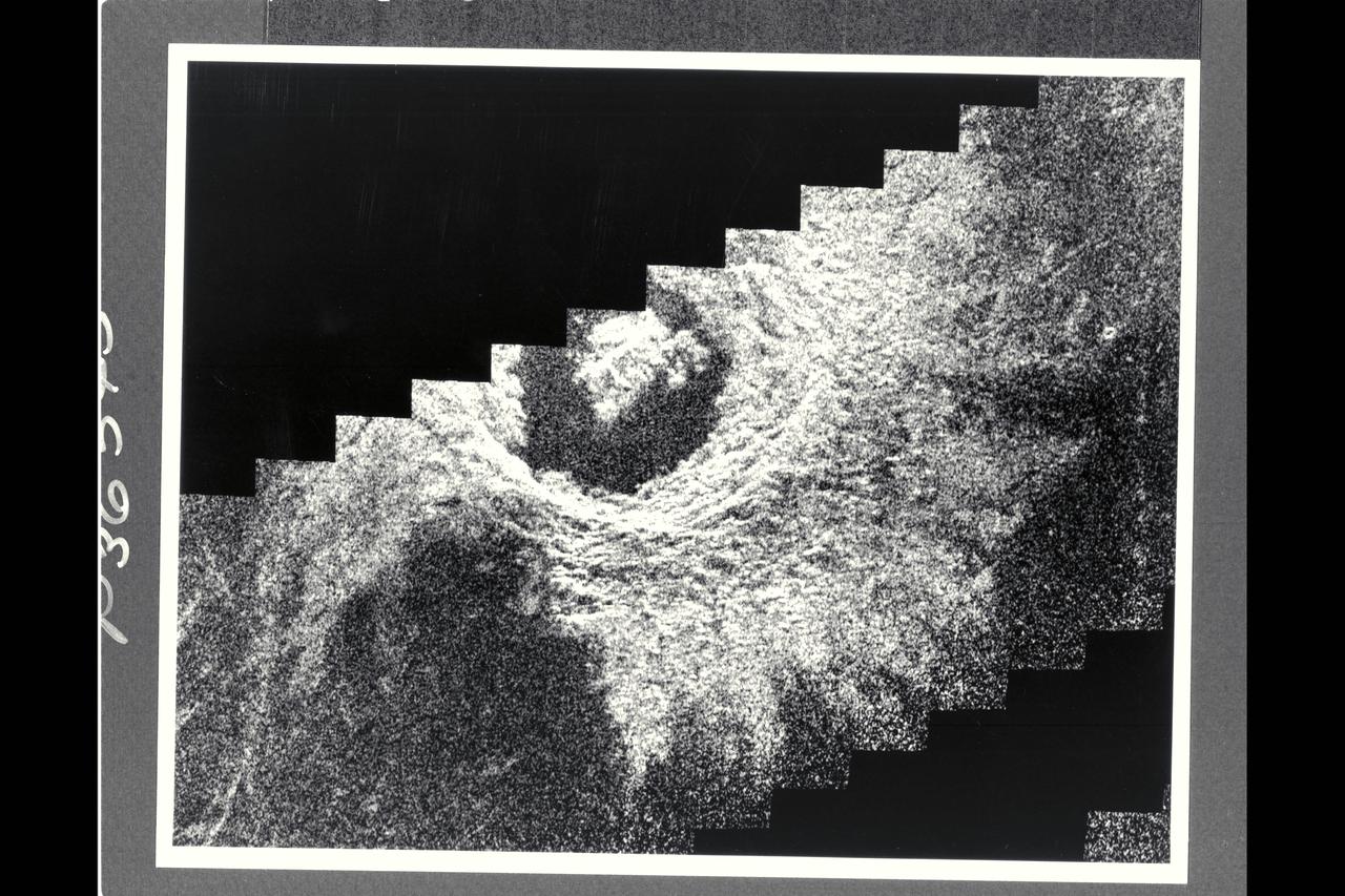 This Magellan image mosaic shows the impact crater Golubkina, first identified in Soviet Venera 15/16 data.  The crater is names after Anna Golubkina (1864-1927), a Soviet sculptor.  The crater is about 34 km (20.4 mi.) across, similar to the size of the West Clearwater impact structure in Canada.  The crater Golubkina is located at about 60.5 degrees north latitude, 286.7 degrees est longitude.  Magellan data reveal that Golubkina has many characteristics typical of craters formed by a mereorite impact including terraced inner walls, a central peak, and radar-bright rough ejecta surrounding the crater.  The extreme darkness of the crater floor indicates a smooth surface, perhaps formed by the ponding of lava flows in the crater floor as seen in may lunar impact craters.  The radar-bright ejecta surrounding the crater indicates a relatively fresh or young crater.  Craters with centeral peaks in the Soviet data range in size from about 10-60 km (6-36 mi.) across.  The largest crater identifed in the Soviet Venera data is 140 km (84 mi) in diameter.  This Magellan image strip in approx. 100 km (62 mi.) long.  The image is a mosaic of two orbits obtained in the first Magellan radar test and played back to Earth to the Deep Space Network stations near Goldstone, CA and Canberra, Australia, respectively.  The resolution of this image is approximately 120 meters (400 feet).  The see-saw margins result from the offset of individual radar frames obtained along the orbit.  The spacecraft moved from the north (top) to the south, looking to the left.