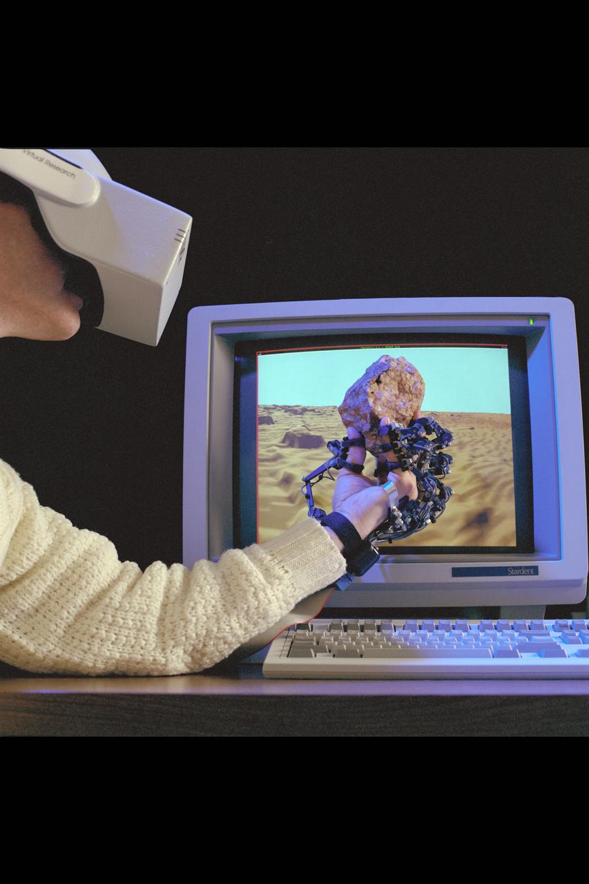 Virtual Environment Telepresence workstation, simulated Mars Exploration shows Dr Michael McGreevy with virtual helmet and EXOS Dexterous interface (holding rock invirtual hand)