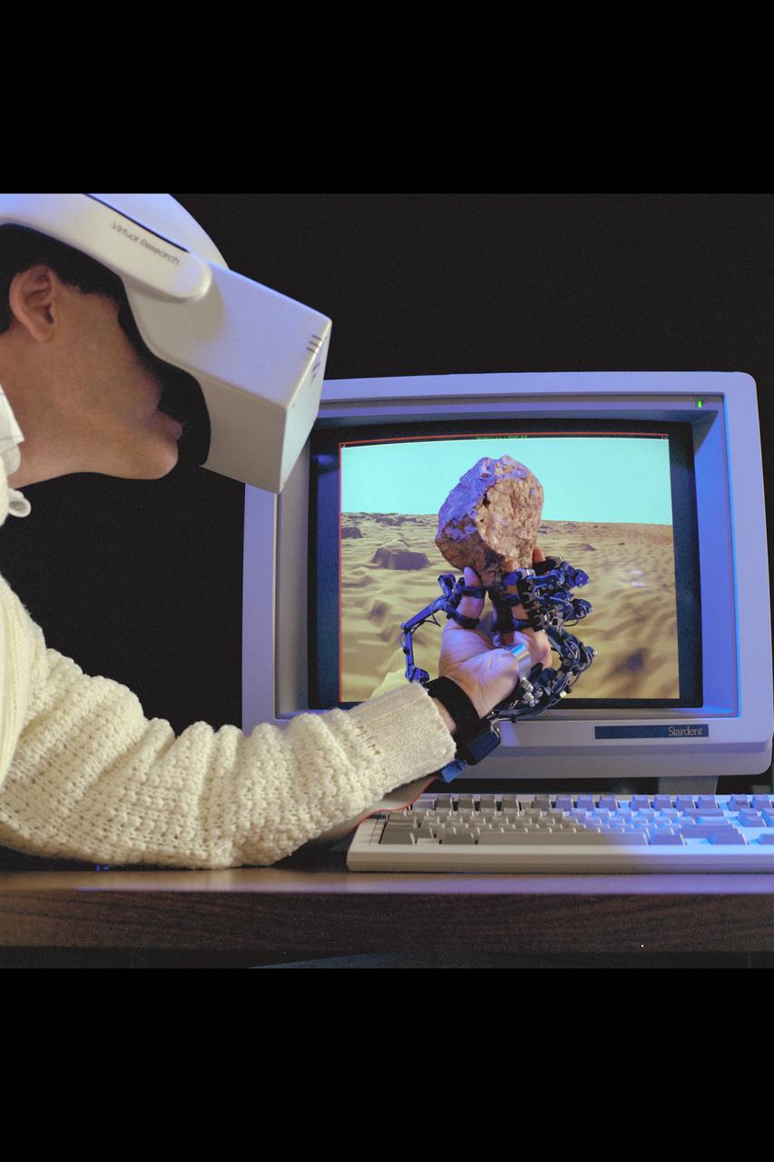 Virtual Environment Telepresence workstation, simulated Mars Exploration shows Dr Michael McGreevy with virtual helmet and EXOS Dexterous interface (holding rock invirtual hand)