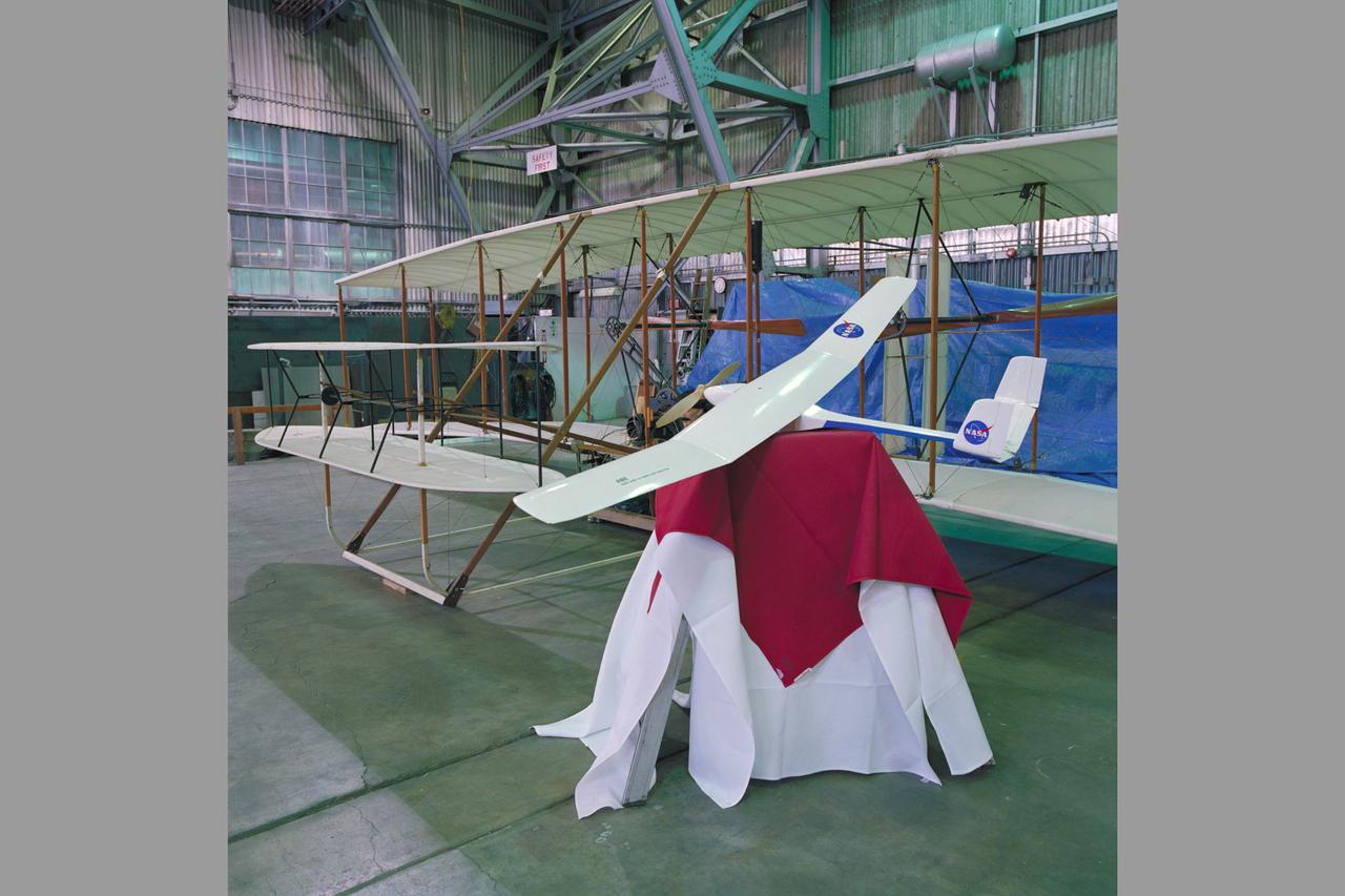 A model of the Ames Mars micromission concept aircraft is shown beside the Wright Flyer replica in the high bay of Ames 40x80ft. wind tunnel