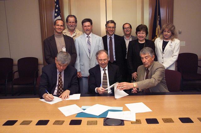 Memorandum of Understanding (MOU) to establish a Unmanned Aerial Vehicles (UAV) Applications Center at NASA Research Park (NRP) was signed into being by (L-R) John Bassett Clark University, Worcester, Mass.,  Dr. Henry McDonald, Director of Ames Research Center and Paul Coleman, Girvan Institute (a non-profit organization lockated in NASA Research Park).  Witnessed by (Back Row, L-R) Steve Douagan, Dave Peterson, Jim Brass, Stan Herwitz, Ken Souza, Estelle Condon, Carolina Blake.