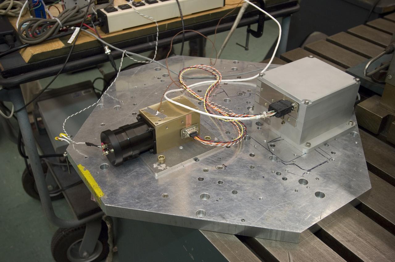 Lunar CRater Observation and Sensing Satellite (LCROSS) and P.I. at NASA Ames Research Center - close up of Total Luminance Photometer:  Metal shake table close up. Shows two units bolted on. The left one is the lens, sensor electronics and photometer sensor. The right is the digital electronics unit for the instrument.  The two units, along with their cabling is one of the LCROSS science insruments.