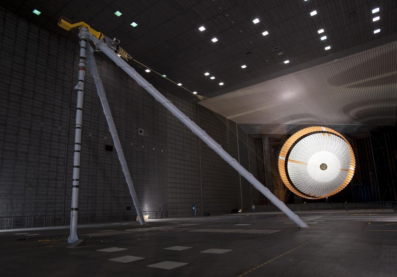 Mars Science Laboratory (MSL) parachuste test in the NASA Ames 80x120ft Subsonic Wind Tunnel at Moffett Field, Calif. (TR #22 - Phase 6) is the largest ever built to fly on an extraterrestrail mission. This image shows a duplicate qualification-test parachute inflated in a  80-mile-per-hour (36-meter-per-second) wind inside the test facility. It has 80 suspension lines, measures more that 50 meers (165 feet) in lenght, and opens to a diameter of nearly 16 meters (51 feet). Most the the orange and white fabric is nylon, though a small disk of heavier polyester is used near the vent in the apex of the canapy due to the higher stresses there.  It is designed to survive deployment at Mach 2.2 in the Martian atmosphere, where it will generate up to 65,000 pounds of drag force.