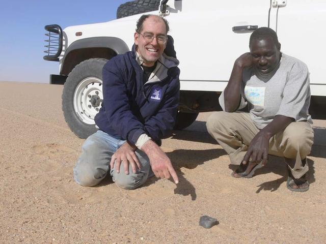 An SUV-sized Asteroid 2008TC# Impacts on October 7, 2008 in the Nubian Desert, Northern Sudan: Dr. Peter Jenniskens, NASA/SETI joined Muawia Shaddas of the University of Khartoum in leading an expedition on a search for samples. (Peter Jenniskens pointing - finds the brick) Photo Credit: NASA/SETI/P. Jenniskens