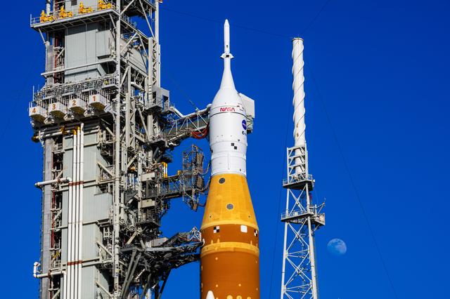 The Moon is seen behind the SLS (Space Launch System) and Orion spacecraft, a...