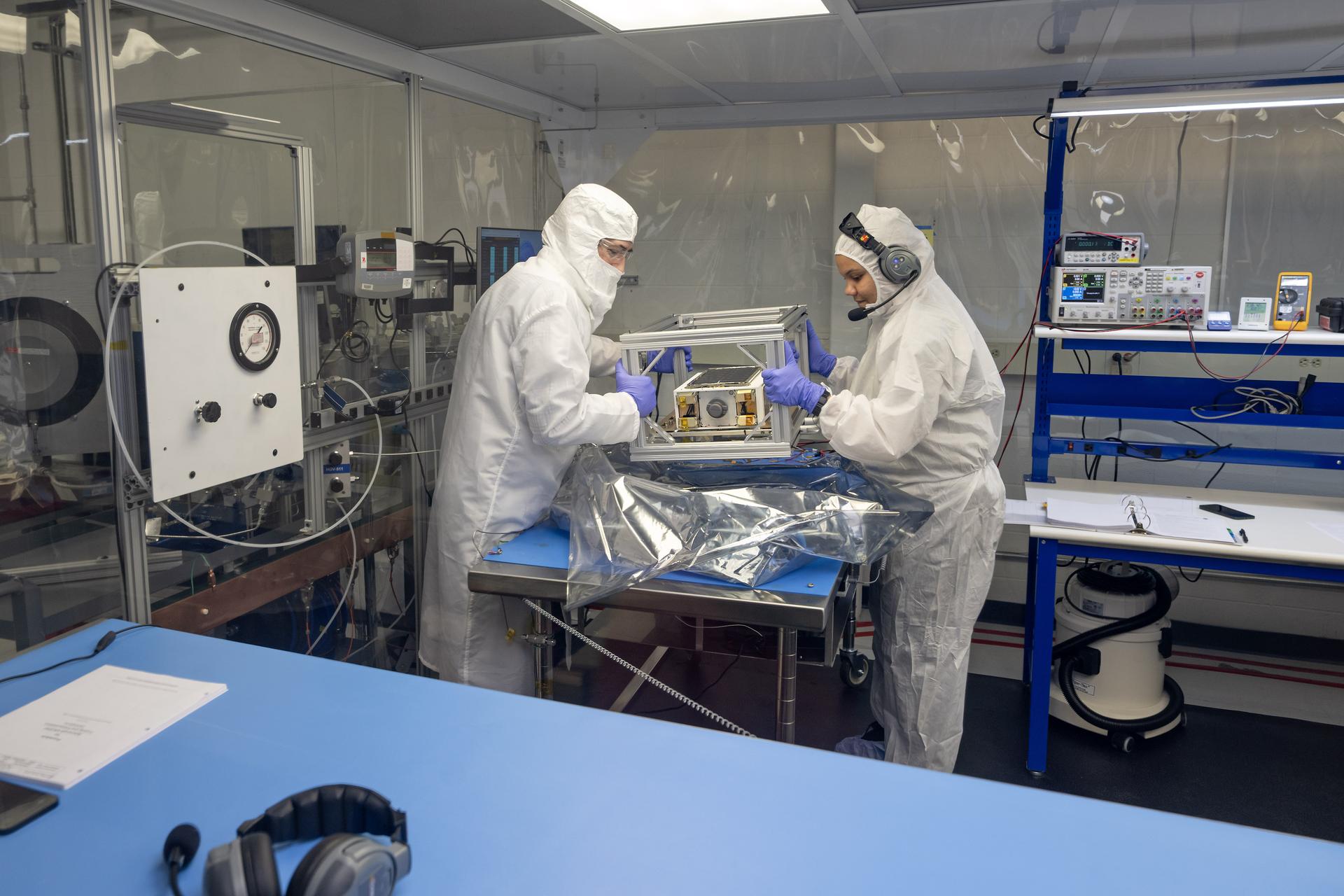 An Album of photos showing NASA engineers and technicians in white protective clean room suits working on a small, rectangular (CubeSat) spacecraft module. They are shown inspecting the hardware on a laboratory workbench, wrapping it in silver foil, and loading it into a large, metallic vacuum chamber at NASA's Marshall Space Flight Center