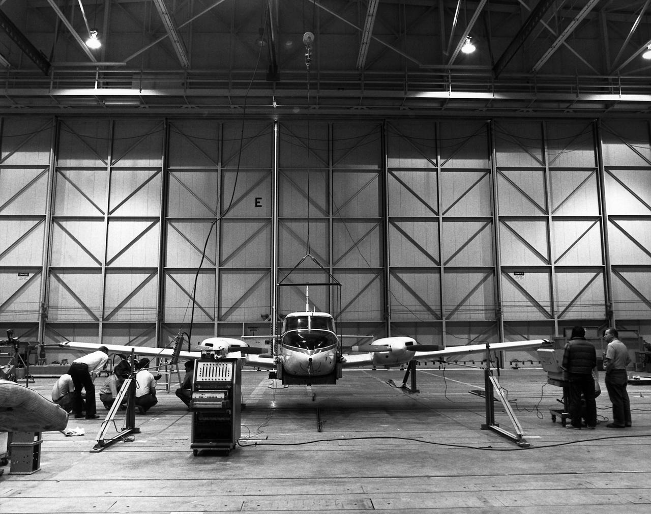 Technicians check instrumentation and systems on NASA 808, a PA-30 aircraft, prior to a research flight. The aircraft was used as the testbed in development of control systems for remotely piloted vehicles that were "flown" from the ground. The concept led to highly successful programs such as the HiMAT and the subscale F-15 remotely piloted vehicles. Over the years, NASA 808 has also been used for spin and stall research related to general aviation aircraft and also research to alleviate wake vortices behind large jetliners.  This 1980 photograph taken inside a hangar shows technicians measuring moment of inertia.