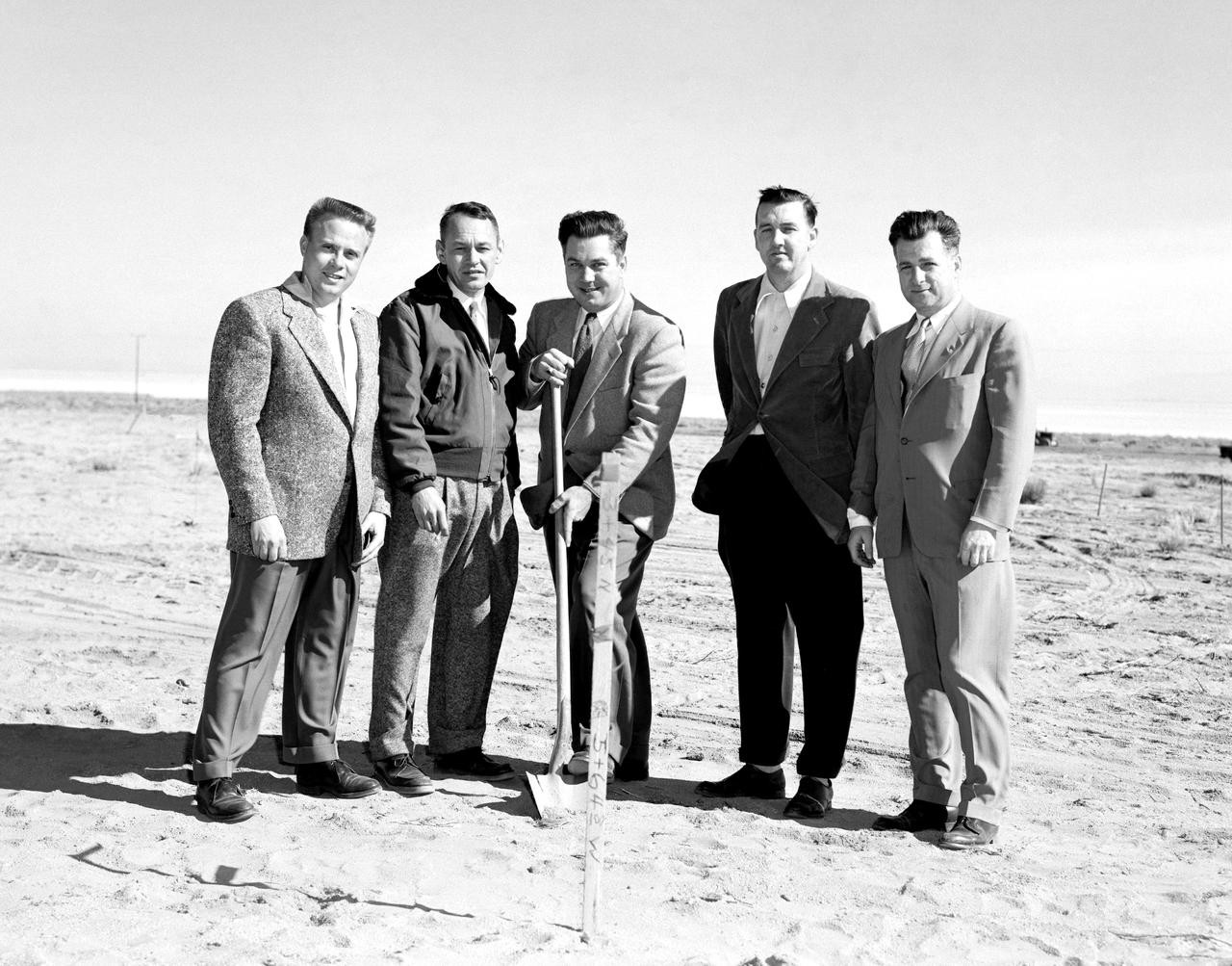 The NACA High-Speed Flight Research Station, had initially been subordinate to the Langley Memorial Aeronautical Laboratory near Hampton, Virginia, but as the flight research in the Mojave Desert increasingly proved its worth after 1946, it made sense to make the Flight Research Station a separate entity reporting directly to the headquarters of the National Advisory Committee for Aeronautics. But an autonomous center required all the trappings of a major research facility, including good quarters. With the adoption of the Edwards “Master Plan,” the Air Force had committed itself to moving from its old South Base to a new location midway between the South and North Bases. The NACA would have to move also--so why not take advantage of the situation and move into a full-blown research facility. The Air Force issued a lease to NACA for a location on the northwestern shore of the Roger Dry Lake. Construction started on the NACA station in early February 1953. On a windy day, January 27, 1953, at a groundbreaking ceremony stood left to right: Gerald Truszynski, Head of Instrumentation Division; Joseph Vensel, Head of the Operations Branch; Walter Williams, Head of the Station, scooping the first shovel full of dirt; Marion Kent, Head of Personnel; and California state official Arthur Samet.