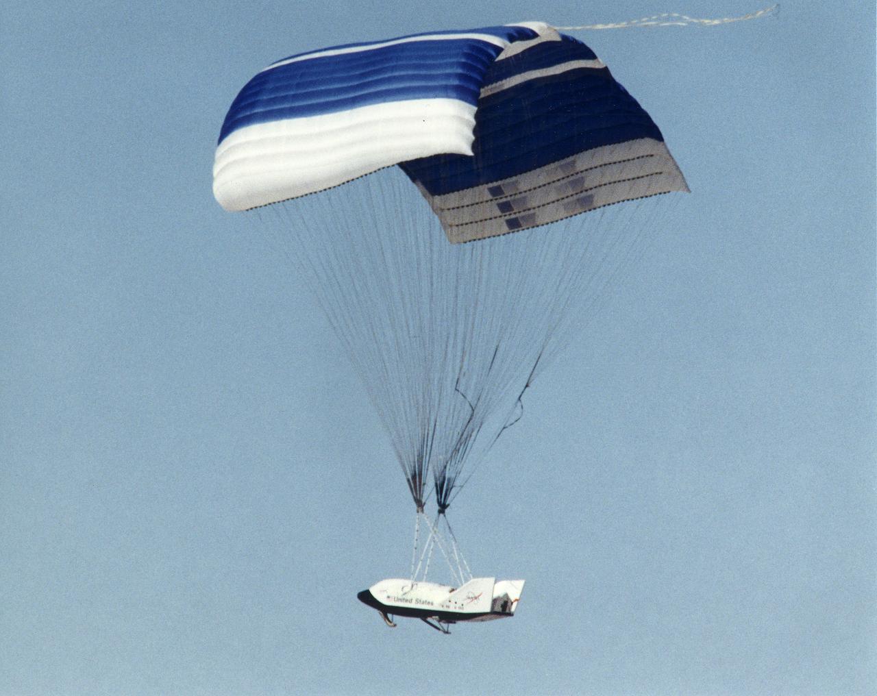 The X-38 technology demonstrator descends under its steerable parafoil toward a lakebed landing in a March 2000 test flight.