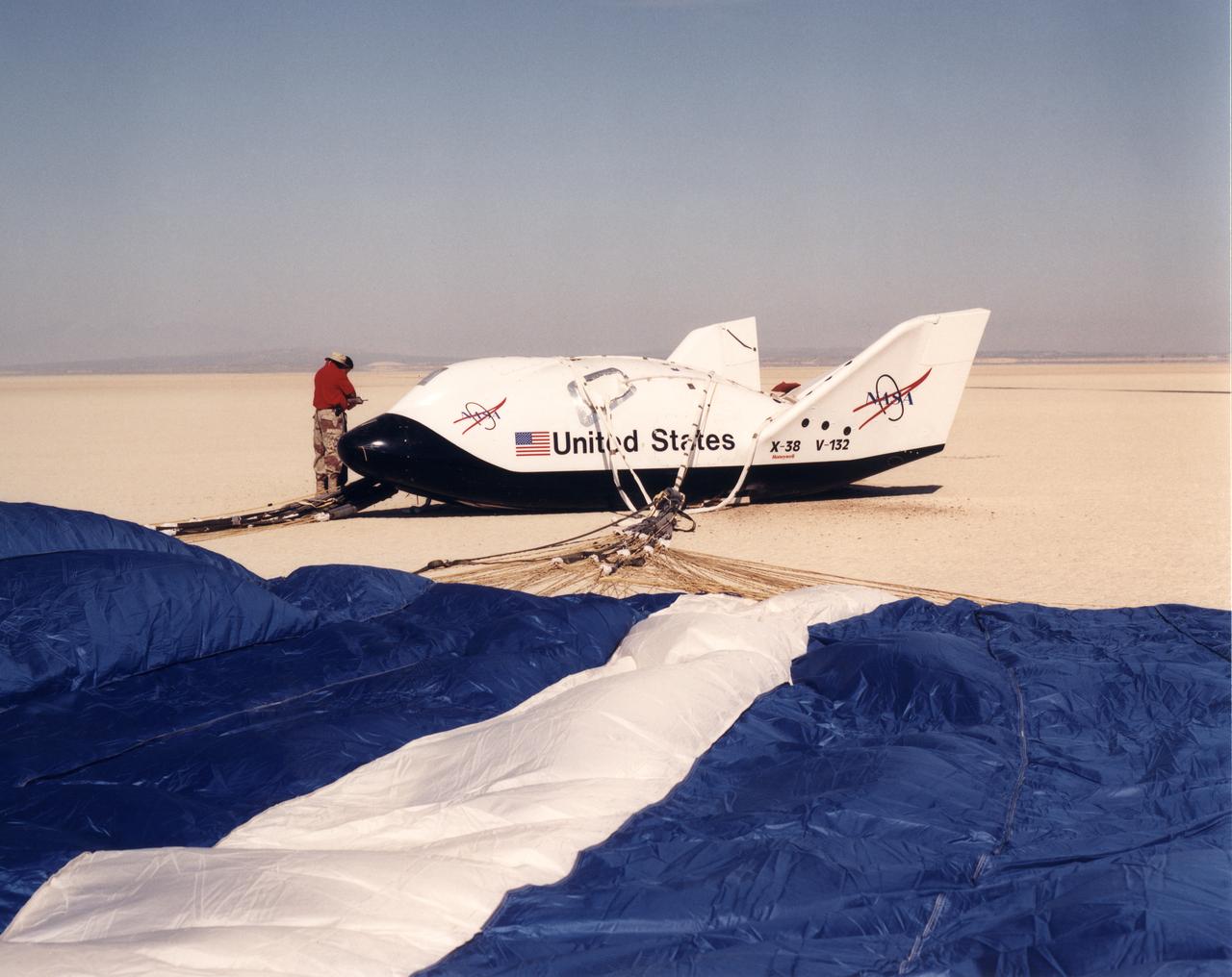 The X-38's blue and white parafoil spreads out in front of the research vehicle as it sits on a lakebed near the Dryden Flight Research Center after a March 2000 test flight.