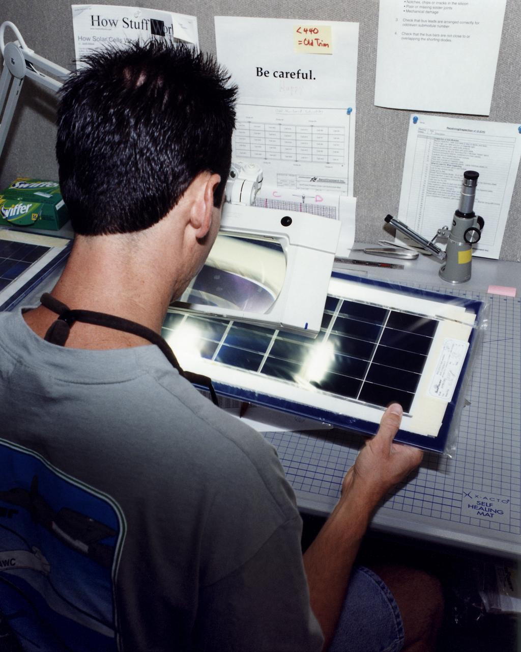 An engineer at AeroVironment's Design Development Center in Simi Valley, California, closely inspects a set of silicon solar cells for potential defects. The cells, fabricated by SunPower, Inc., of Sunnyvale, California, are among 64,000 solar cells which have been installed on the Helios Prototype solar-powered aircraft to provide power to its 14 electric motors and operating systems.