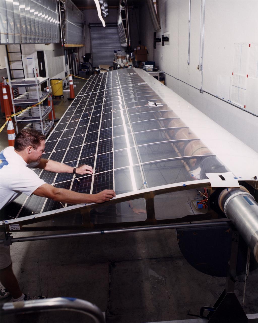 Technician Marshall MacCready carefully lays a panel of solar cells into place on a wing section of the Helios Prototype flying wing at AeroVironment's Design Development Center in Simi Valley, California. The bi-facial cells, manufactured by SunPower, Inc., of Sunnyvale, California, are among 64,000 solar cells which have been installed on the solar-powered aircraft to provide electricity to its 14 motors and operating systems.