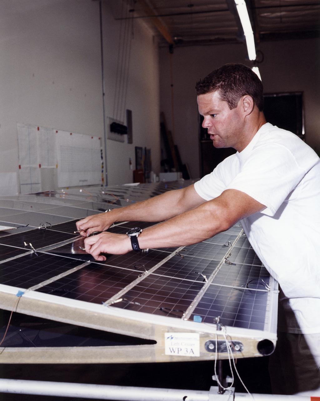 Technician Marshall MacCready carefully lays a panel of solar cells into place on a wing section of the Helios Prototype flying wing at AeroVironment's Design Development Center in Simi Valley, California. More than 1,800 panels containing some 64,000 bi-facial cells, fabricated by SunPower, Inc., of Sunnyvale, California, have been installed on the solar-powered aircraft to provide electricity to its 14 motors and operating systems.