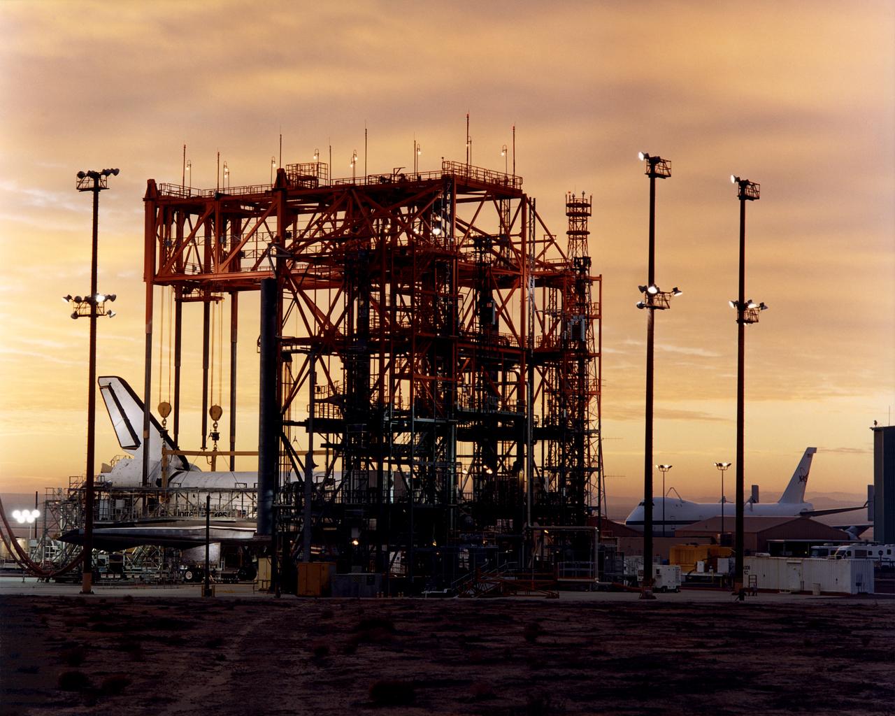 The early-morning Sun provides a golden backdrop to the Space Shuttle Discovery encased in the Mate-Demate Device (MDD) at NASA’s Dryden Flight Research Center at Edwards, California. The gantry-like MDD structure is used to prepare the shuttle for its ferry flight back to the Kennedy Space Center in Florida, including mounting the shuttle atop NASA’s modified Boeing 747 Shuttle Carrier Aircraft.