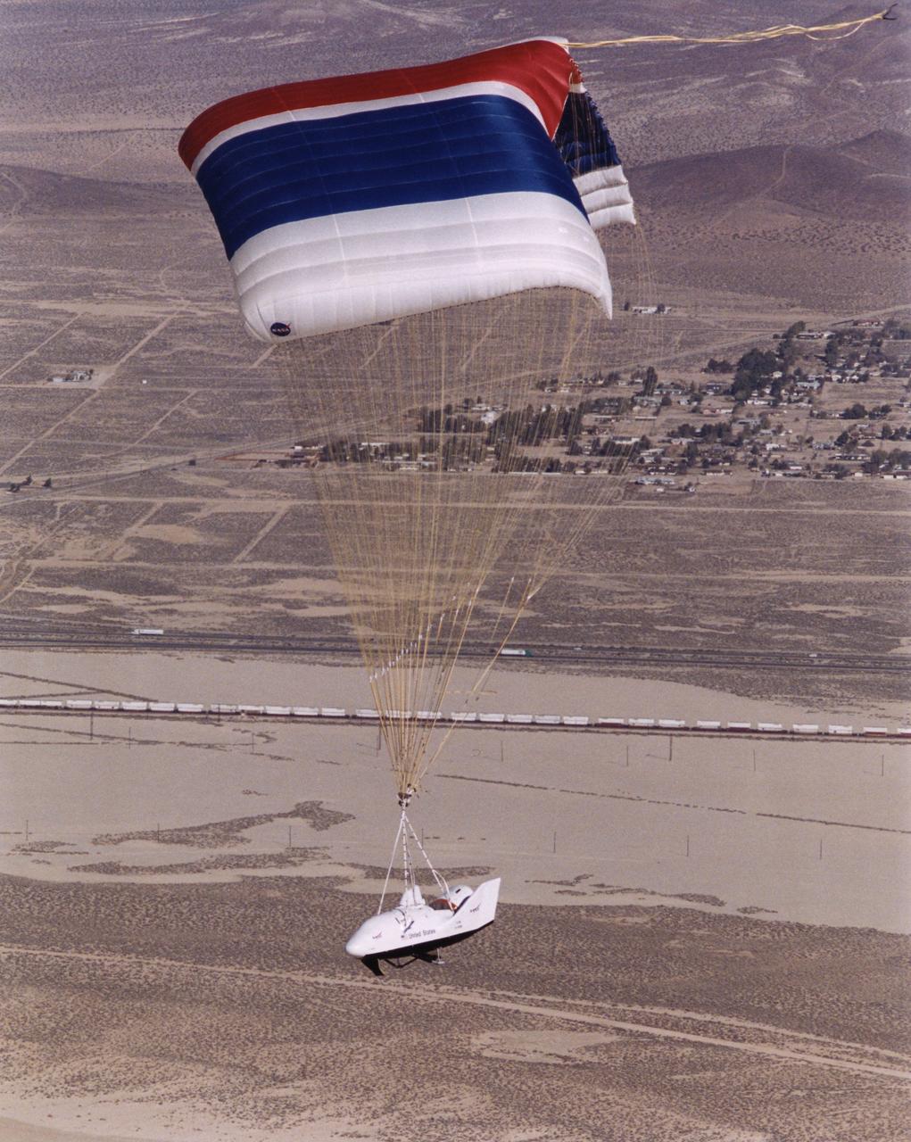 The third iteration of the X-38, V-131R, glides down under a giant parafoil towards a landing on Rogers Dry Lake near NASAÕs Dryden Flight Research Center during its first free flight Nov. 2, 2000. The X-38 prototypes are intended to perfect technology for a planned Crew Return Vehicle (CRV) ÒlifeboatÓ to carry a crew to safety in the event of an emergency on the International Space Station. Free-flight tests of X-38 V-131R are evaluating upgraded avionics and control systems and the aerodynamics of the modified upper body, which is more representative of the final design of the CRV than the two earlier X-38 test craft, including a simulated hatch atop the body. The huge 7,500 square-foot parafoil will enable the CRV to land in the length of a football field after returning from space. The first three X-38Õs are air-launched from NASAÕs venerable NB-52B mother ship, while the last version, V-201, will be carried into space by a Space Shuttle and make a fully autonomous re-entry and landing.