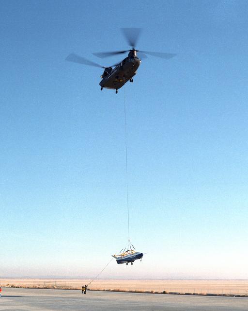 NASA image: Ground crewmen help guide the alignment of the X-40A as the experimental craft is gently lowered to the ground by a U.S. Army CH-47 Chinook helicopter following a captive-carry test flight