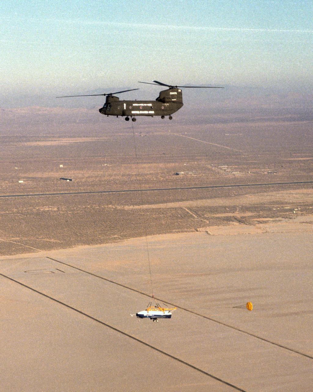 The X-40 sub-scale technology demonstrator and its U.S. Army CH-47 Chinook helicopter mothership fly over a dry lakebed runway during a captive-carry test flight from NASA's Dryden Flight Research Center, Edwards, California. The X-40 is attached to a sling which is suspended from the CH-47 by a 110-foot-long cable during the tests, while a small parachute trails behind to provide stability. The captive carry flights are designed to verify the X-40's navigation and control systems, rigging angles for its sling, and stability and control of the helicopter while carrying the X-40 on a tether. Following a series of captive-carry flights, the X-40 made free flights from a launch altitude of about 15,000 feet above ground, gliding to a fully autonomous landing. The X-40 is an unpowered 82 percent scale version of the X-37, a Boeing-developed spaceplane designed to demonstrate various advanced technologies for development of future lower-cost access to space vehicles.