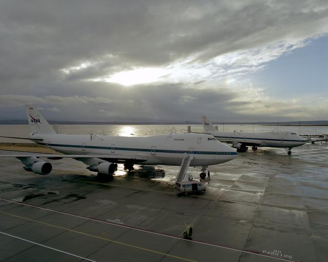 NASA image: The sun begins to break through the clouds over NASA's two 747 Shuttle Carrier Aircraft on the NASA Dryden ramp after a rain shower in February 2001